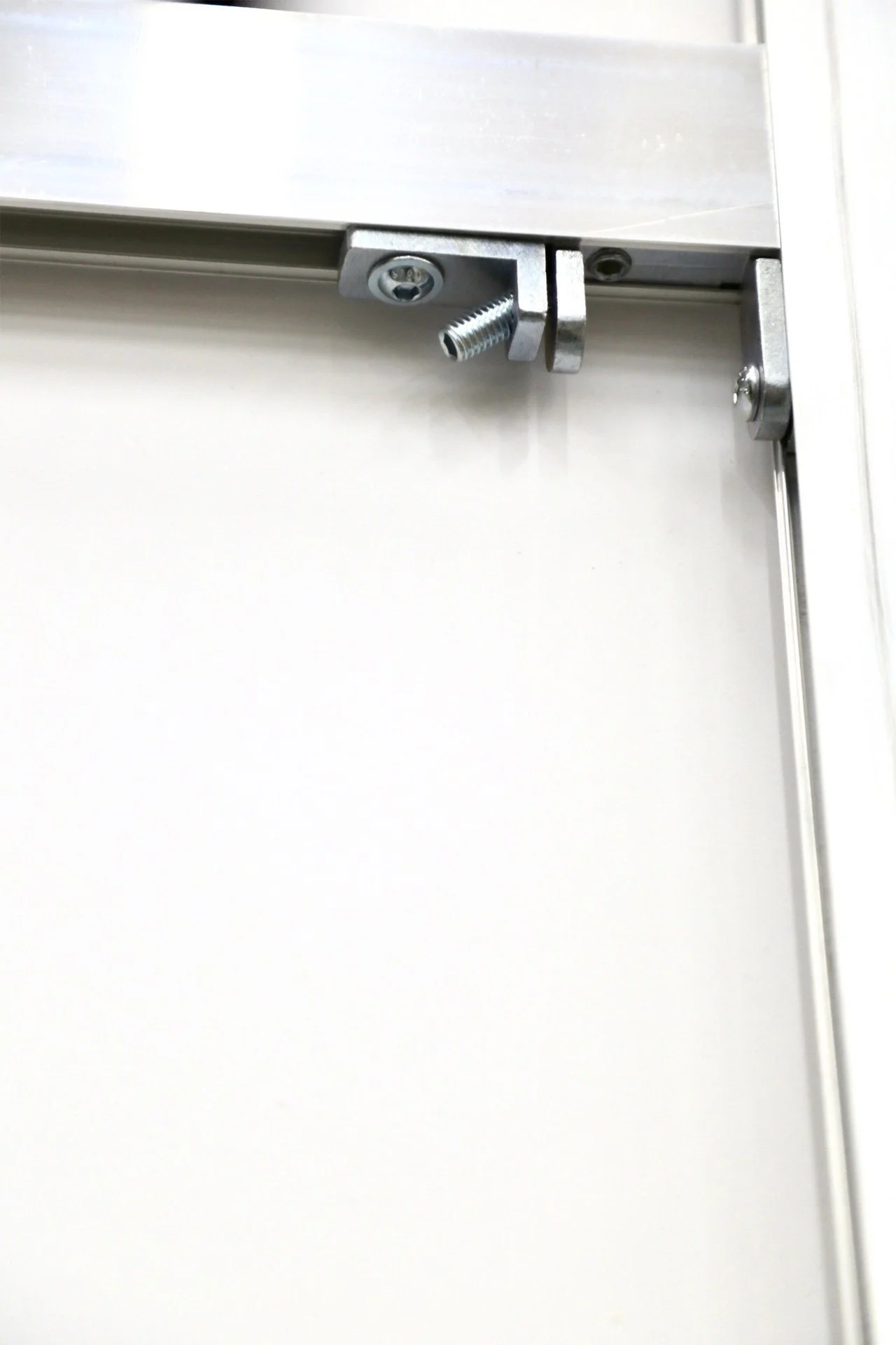 A close-up of a metal latch mechanism on a white door or panel, including screws and a threaded bolt.