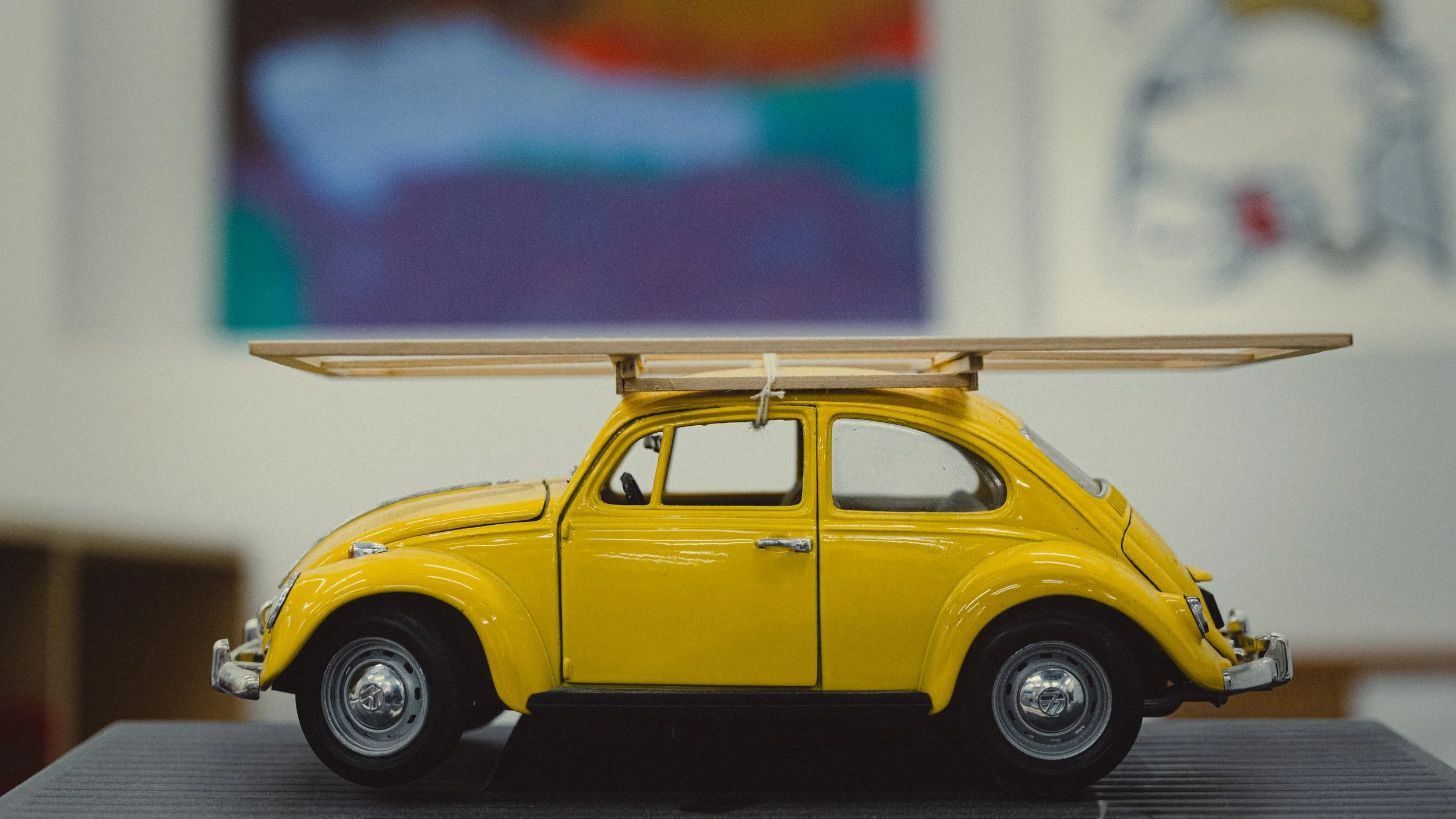 Close-up of a yellow toy Volkswagon VW beetle with a wooden stretcher tied on top.