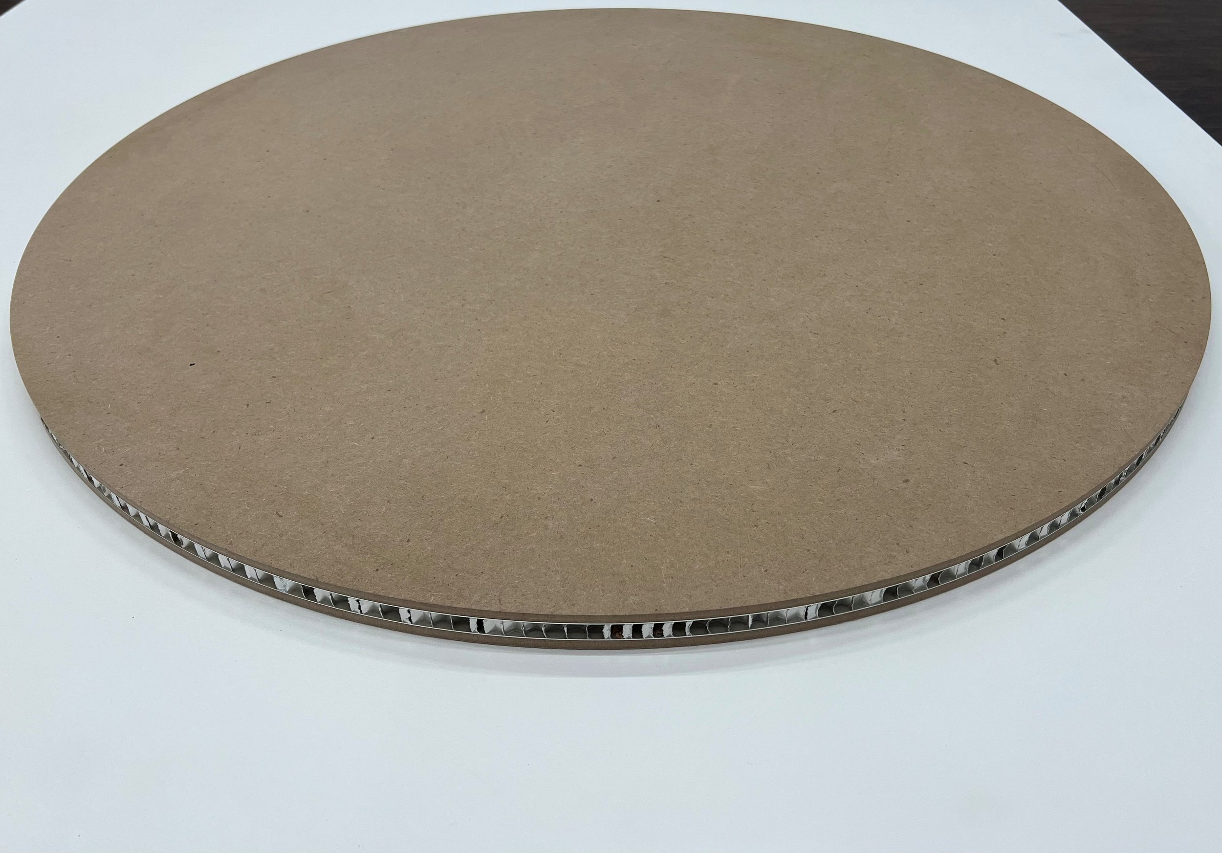 Close-up of a tondo art panel with an exposed honeycomb core (grooved edge), placed on a white surface.