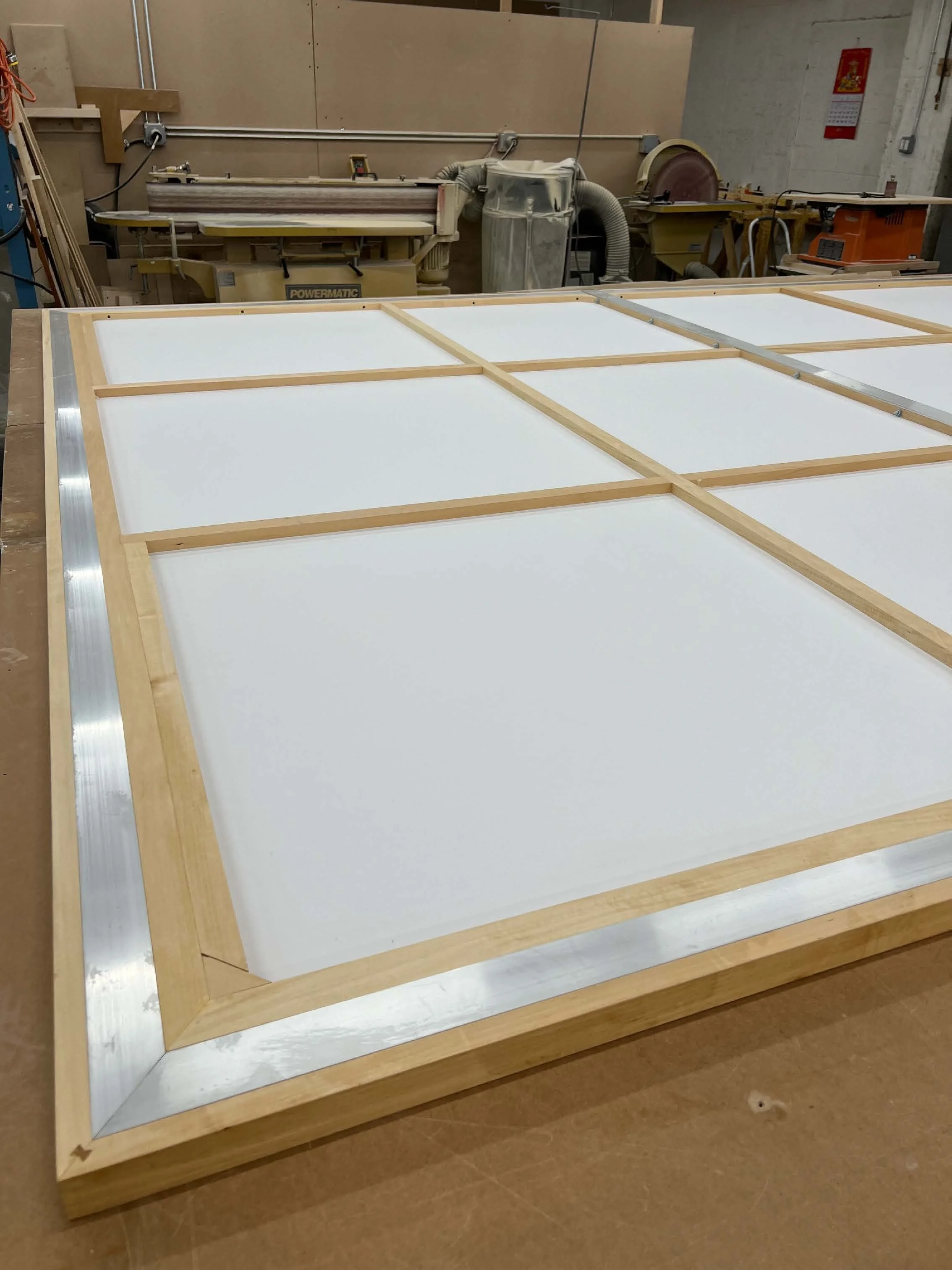 A large wooden Dibond panel with Aluminum extrustion inset, placed in a workshop with various woodworking equipment in the background.