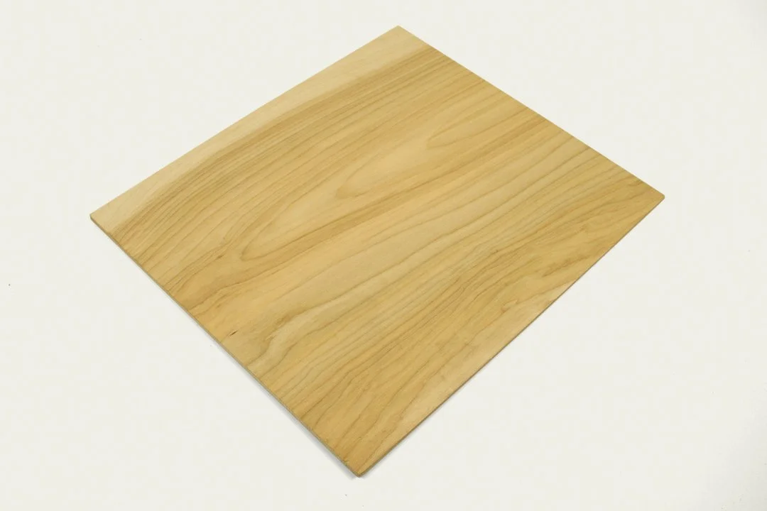 A square piece of light-colored wood or laminate with a smooth surface, positioned on a plain white background.