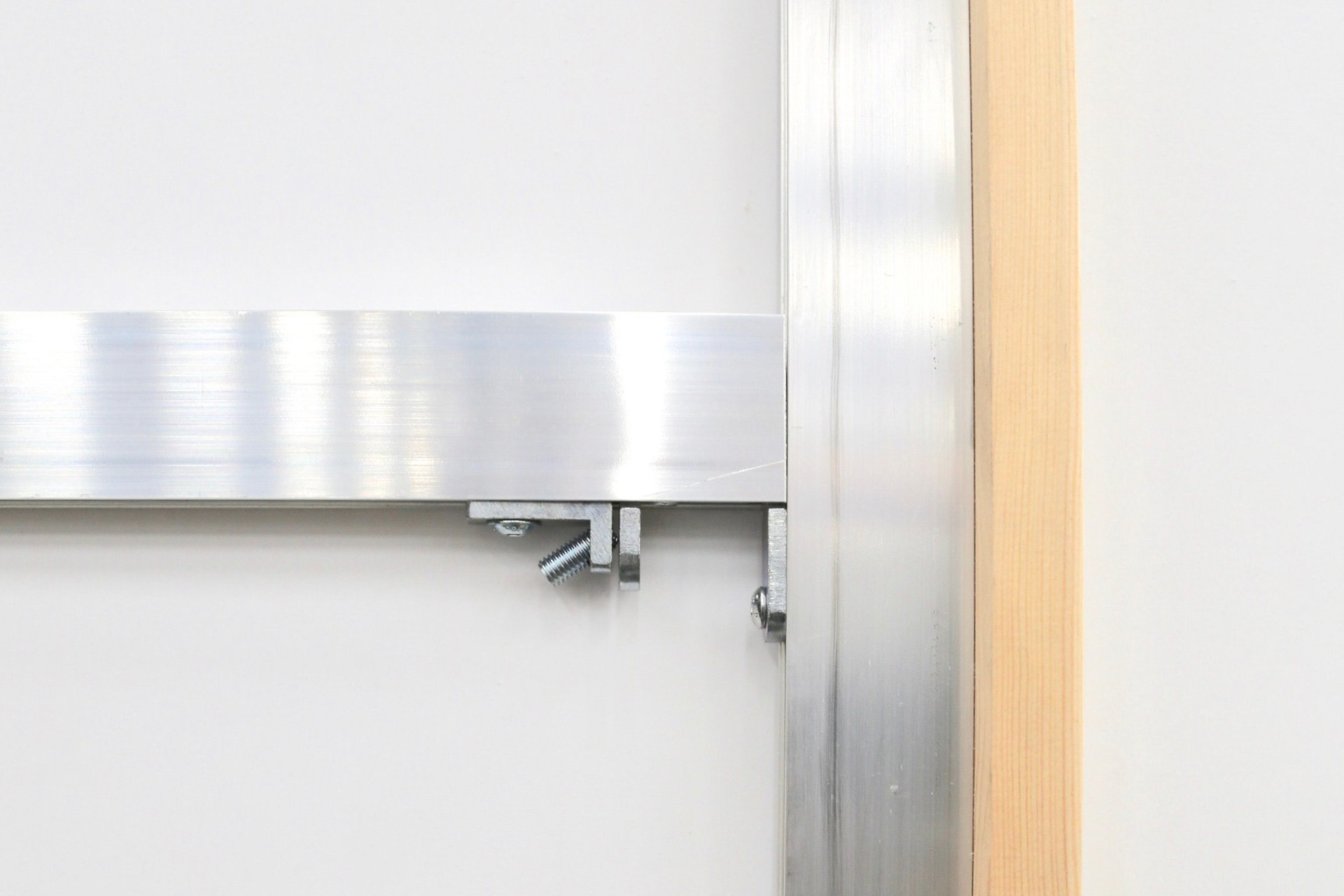 Close-up of metal hardware attached to a white wall with a wooden trim on the right side.