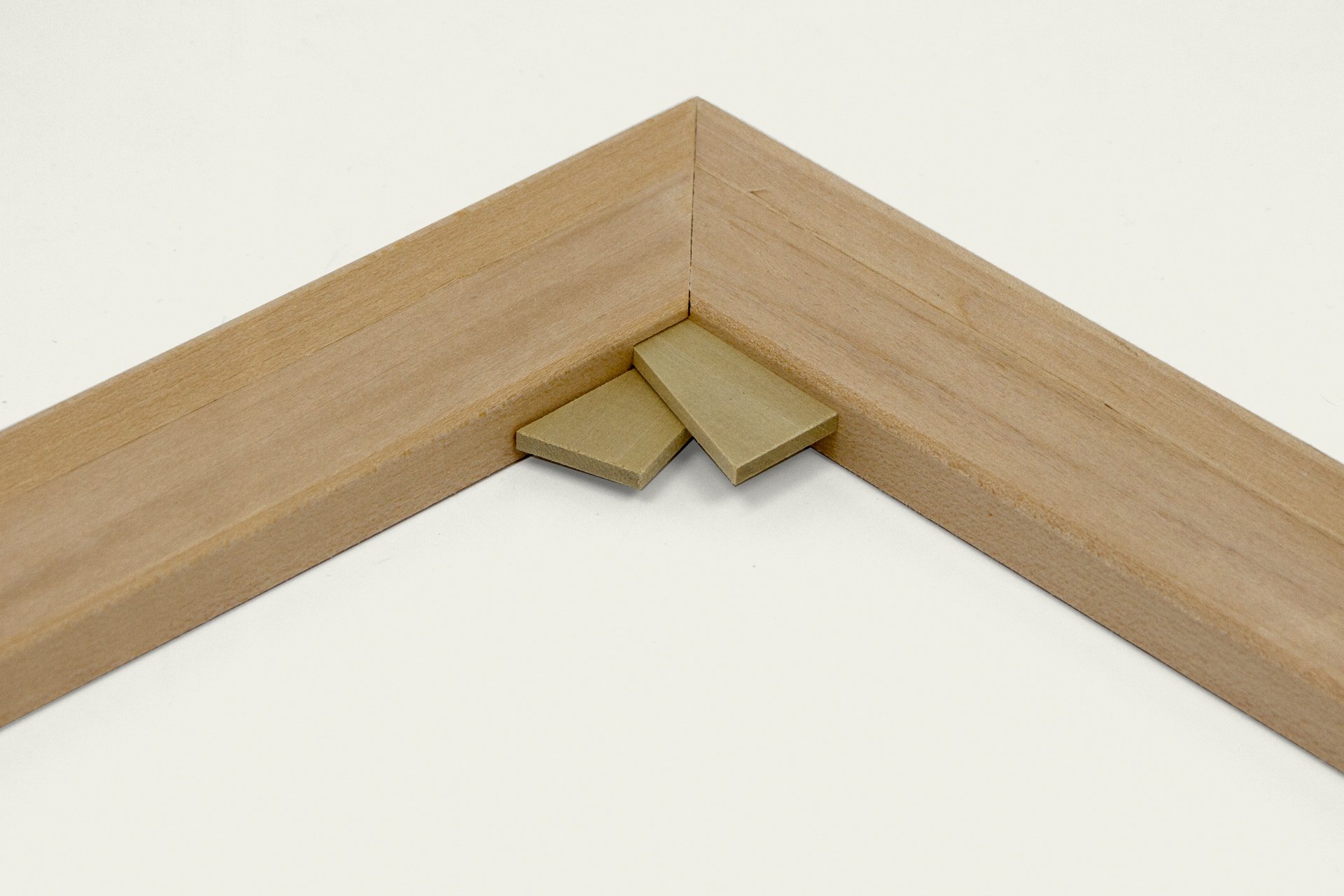 Close-up of two wooden pieces joined at a 90-degree angle with two small rectangular wooden blocks inserted at the joint, on a white background.