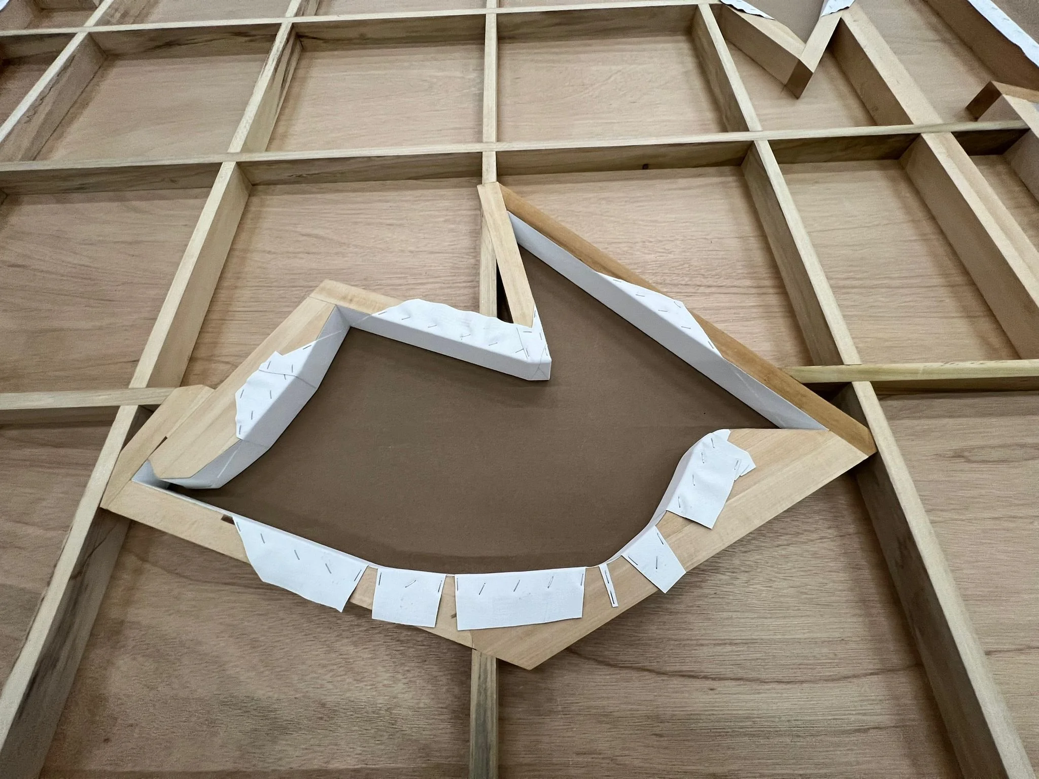 Wooden furniture parts laid out on a surface, including strips, frames, and decorative elements, with paper templates attached.
