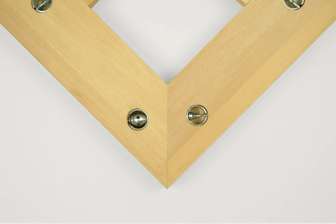 Close-up of a wooden picture frame corner with metal attachment hardware on a white surface.