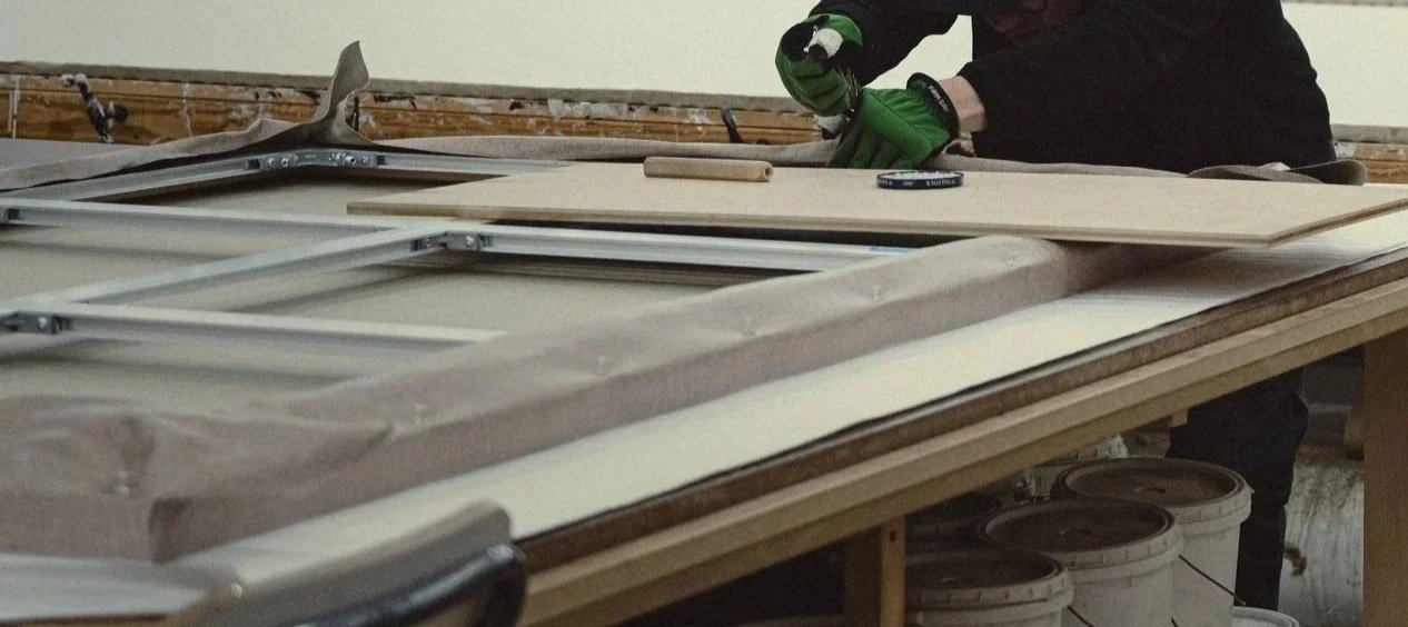 Person working on a woodworking project, stretching a canvas using tool on a large workbench on an aluminum stretcher.