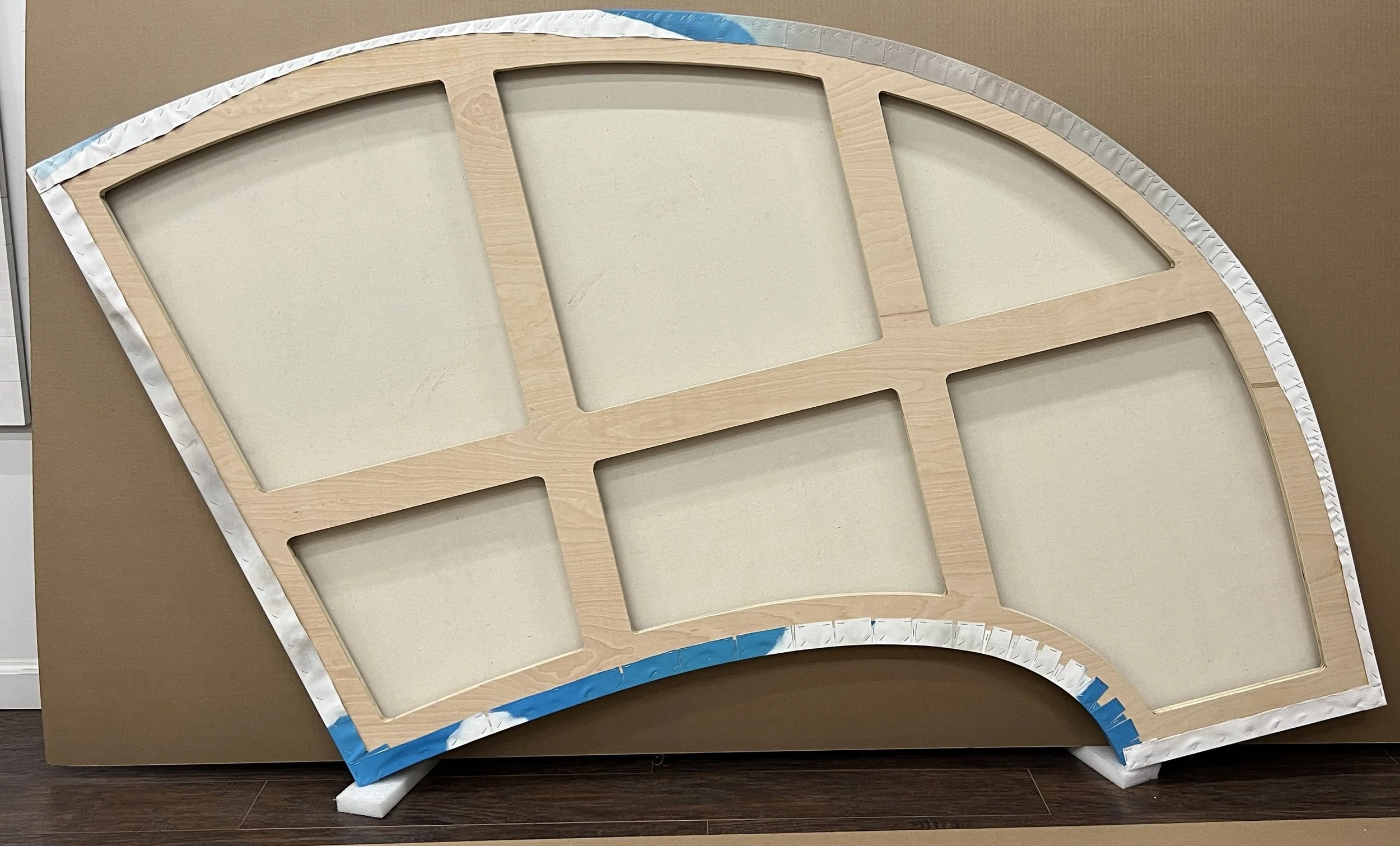 Large wooden rainbow-shaped display with multiple empty rectangular cutouts, blue and silver edging, and brown background.