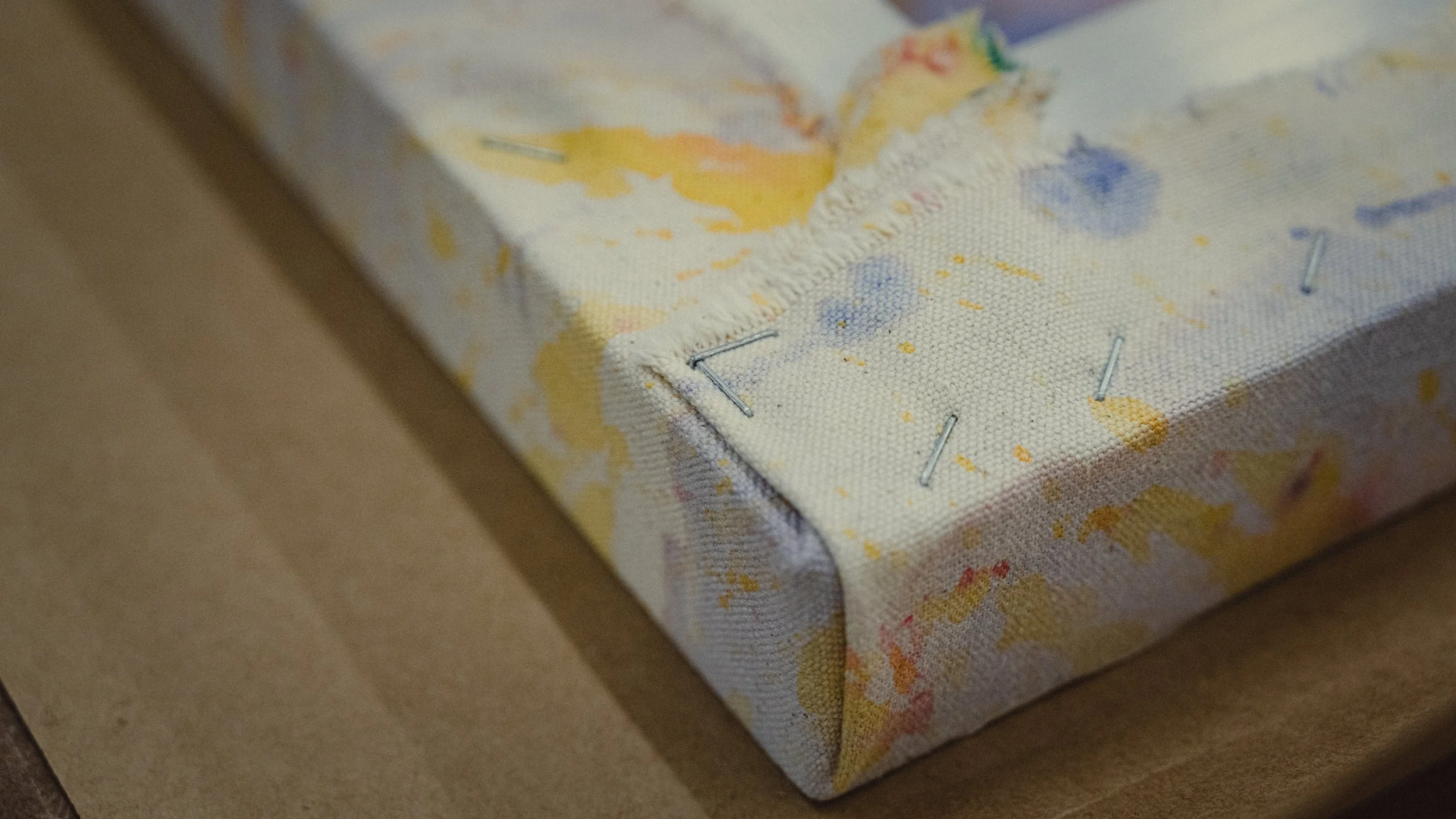 Close-up of a corner of a stretched painting secured with small staples by Simon Liu.