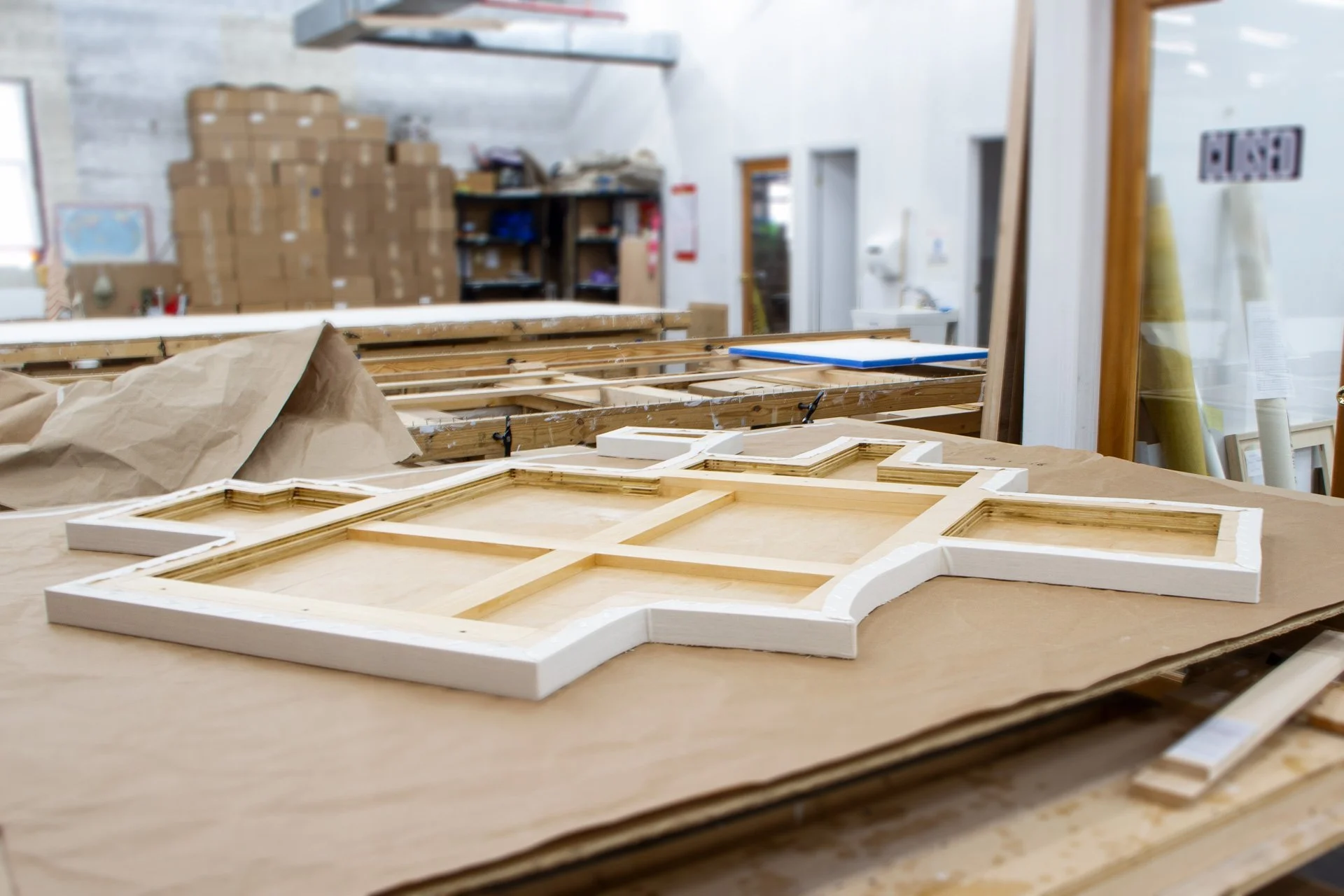 Wooden and white moldings on a worktable with background storage shelves and cardboard boxes.
