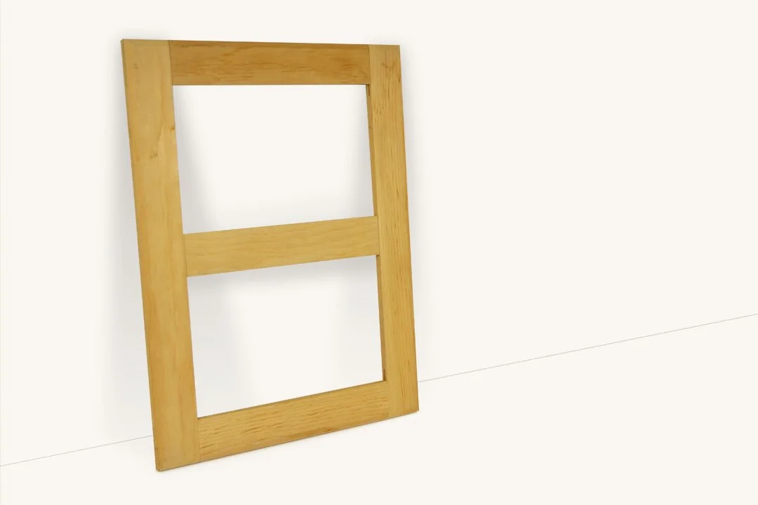 A wooden window frame leaning against a white wall.