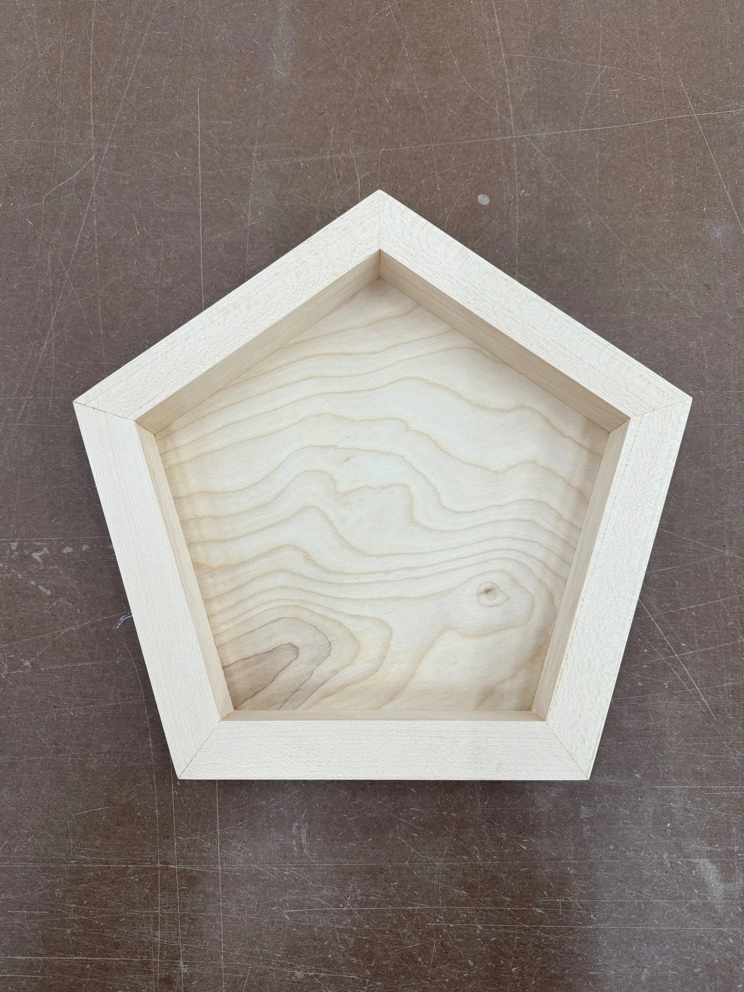 Close-up view of an empty hexagonal wooden art panel on a dark work table.