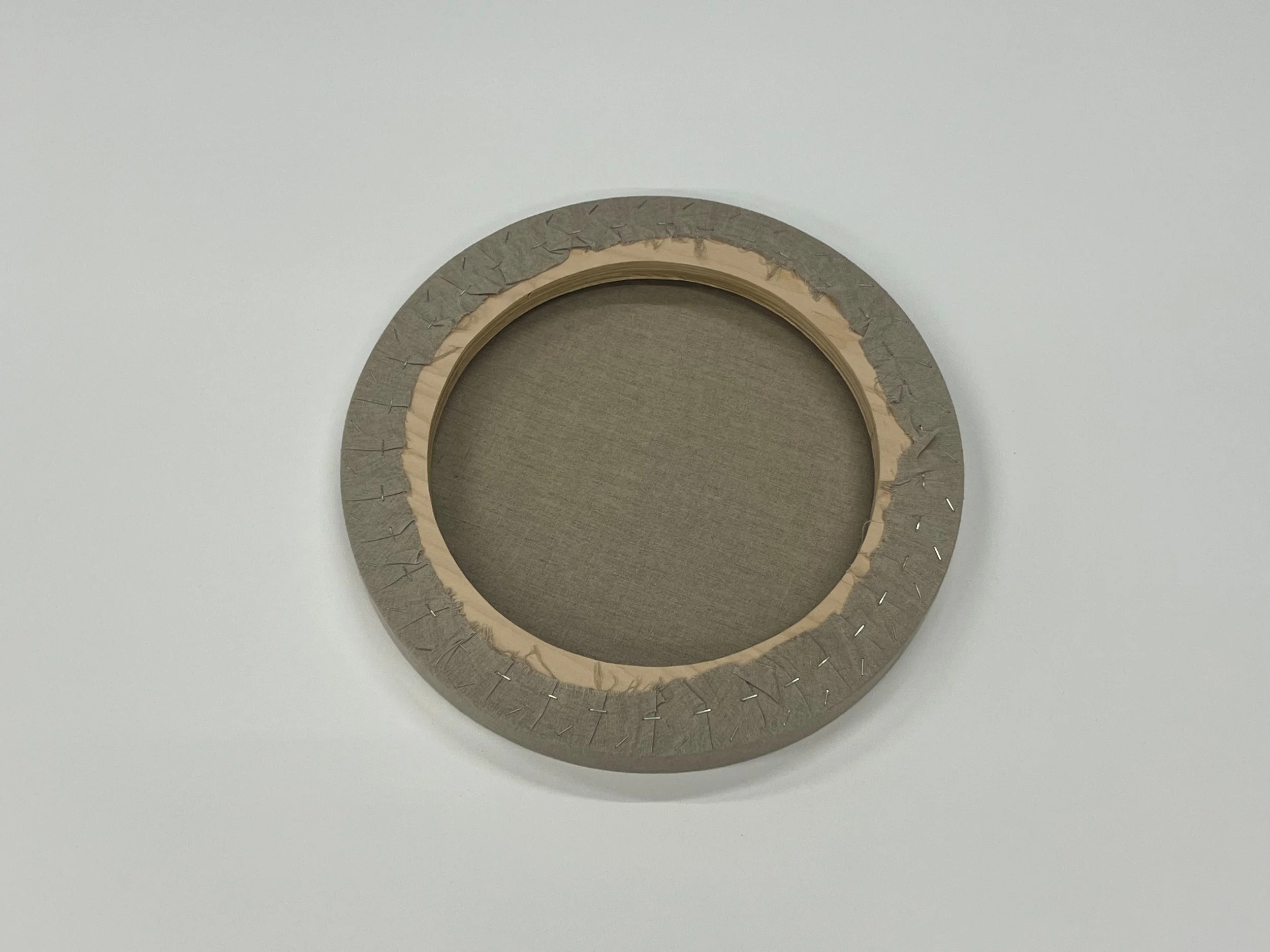 A circular embroidery hoop with batting and fabric stretched in it. The outer edge of the hoop is padded with fabric and secured with pins.