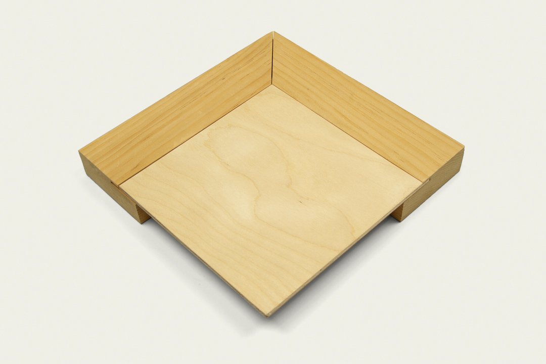 A square wooden tray with raised sides, made of light-colored wood, on a white surface.