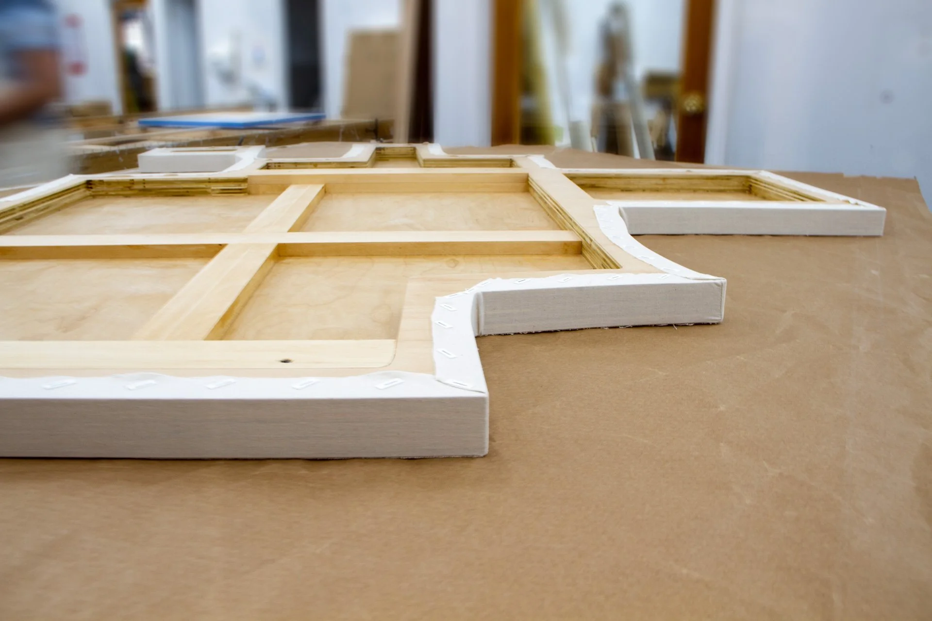 Wooden picture frame with white border resting on a tan work surface in a workshop.