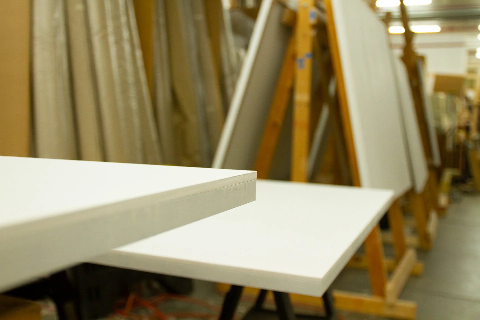 White gessoed panels in a woodworking shop with display racks and wooden art supports in the background.