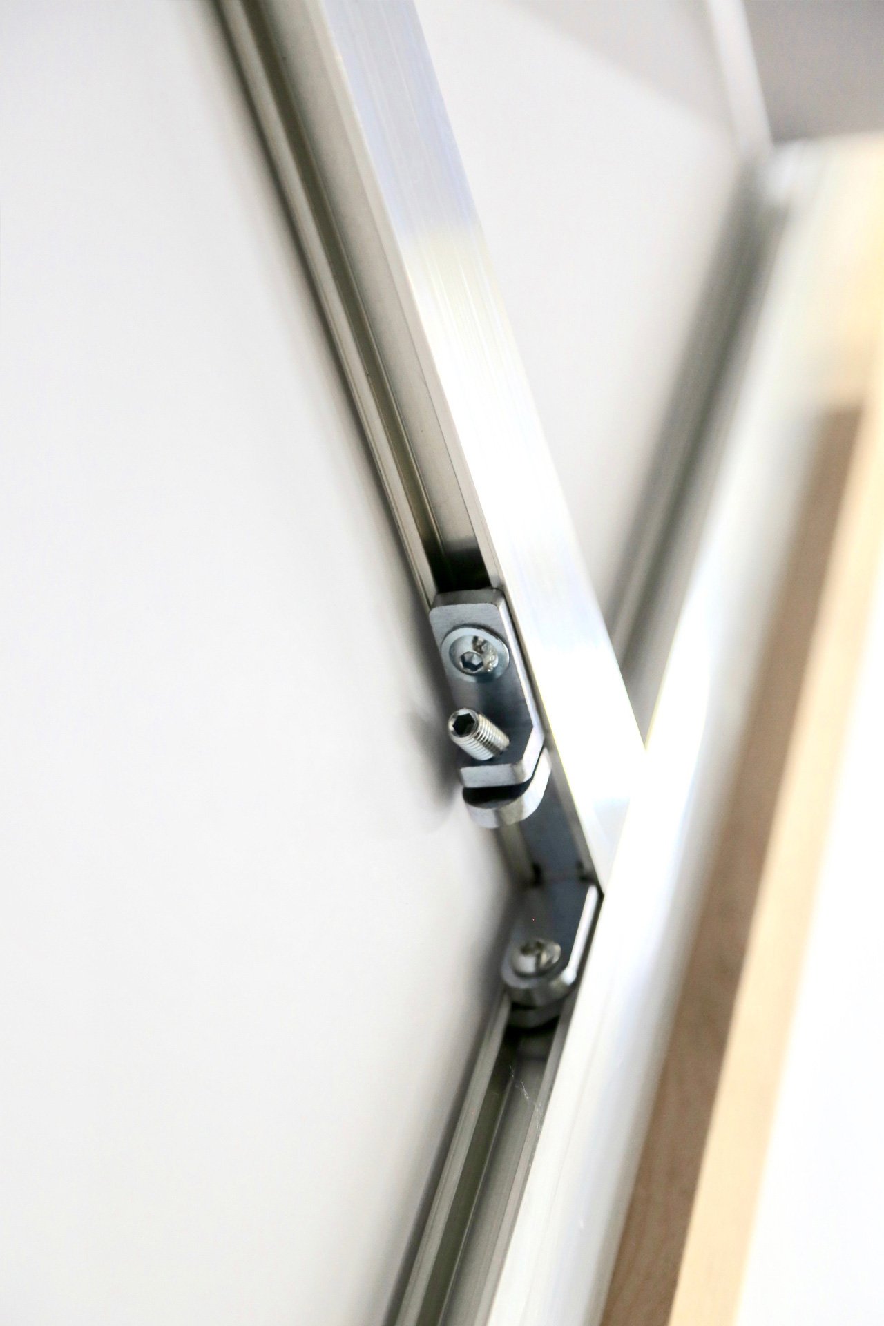 Close-up view of a metal hinge or latch mechanism attached to a white surface, possibly part of a door or window frame.