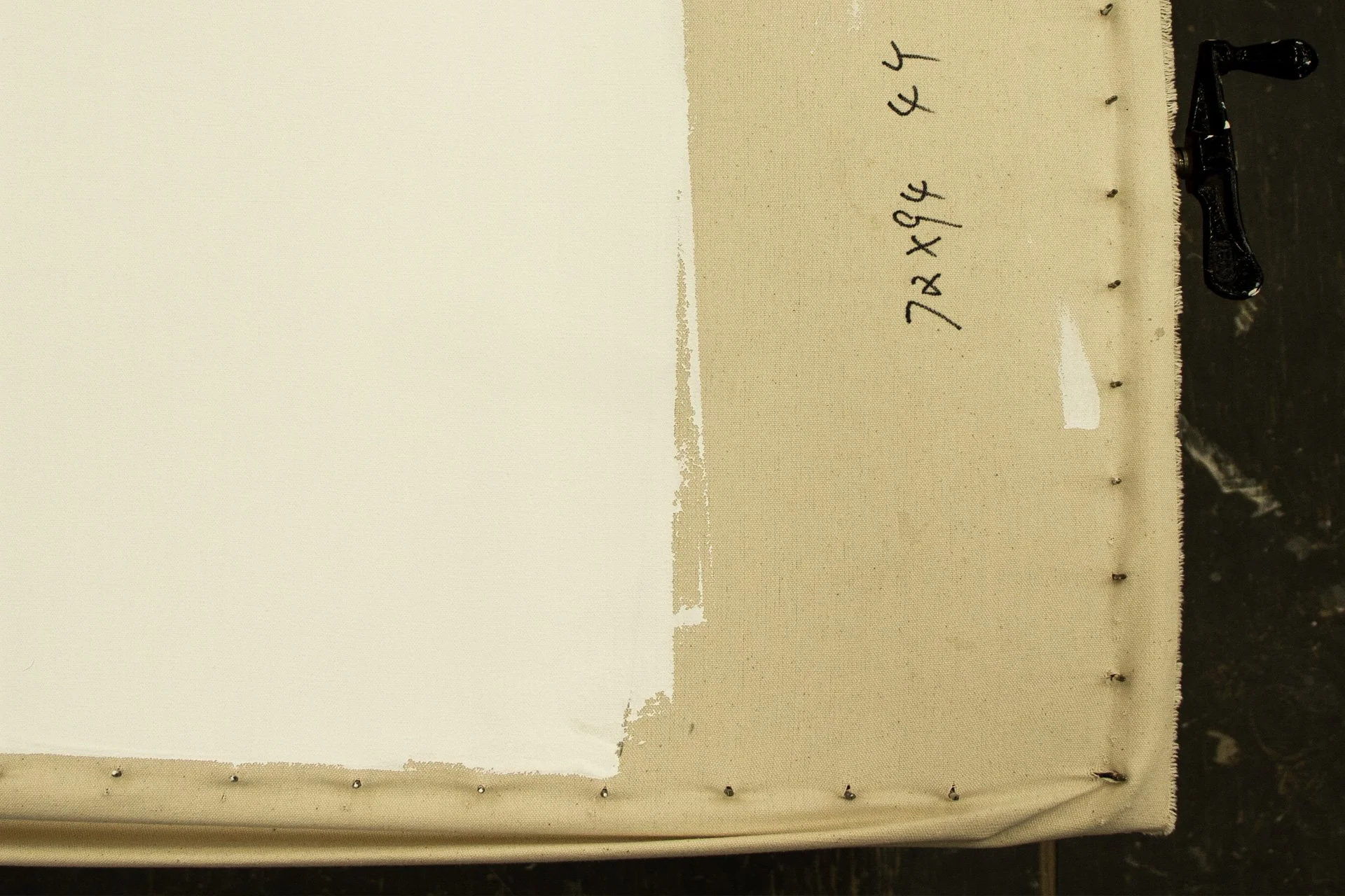 Close-up of a fabric surface with handwritten mathematical expressions: 7x + 4 and 4x + 4. The fabric is sewn around the edges with small metal staples, and a metal clamp is visible on the right side.