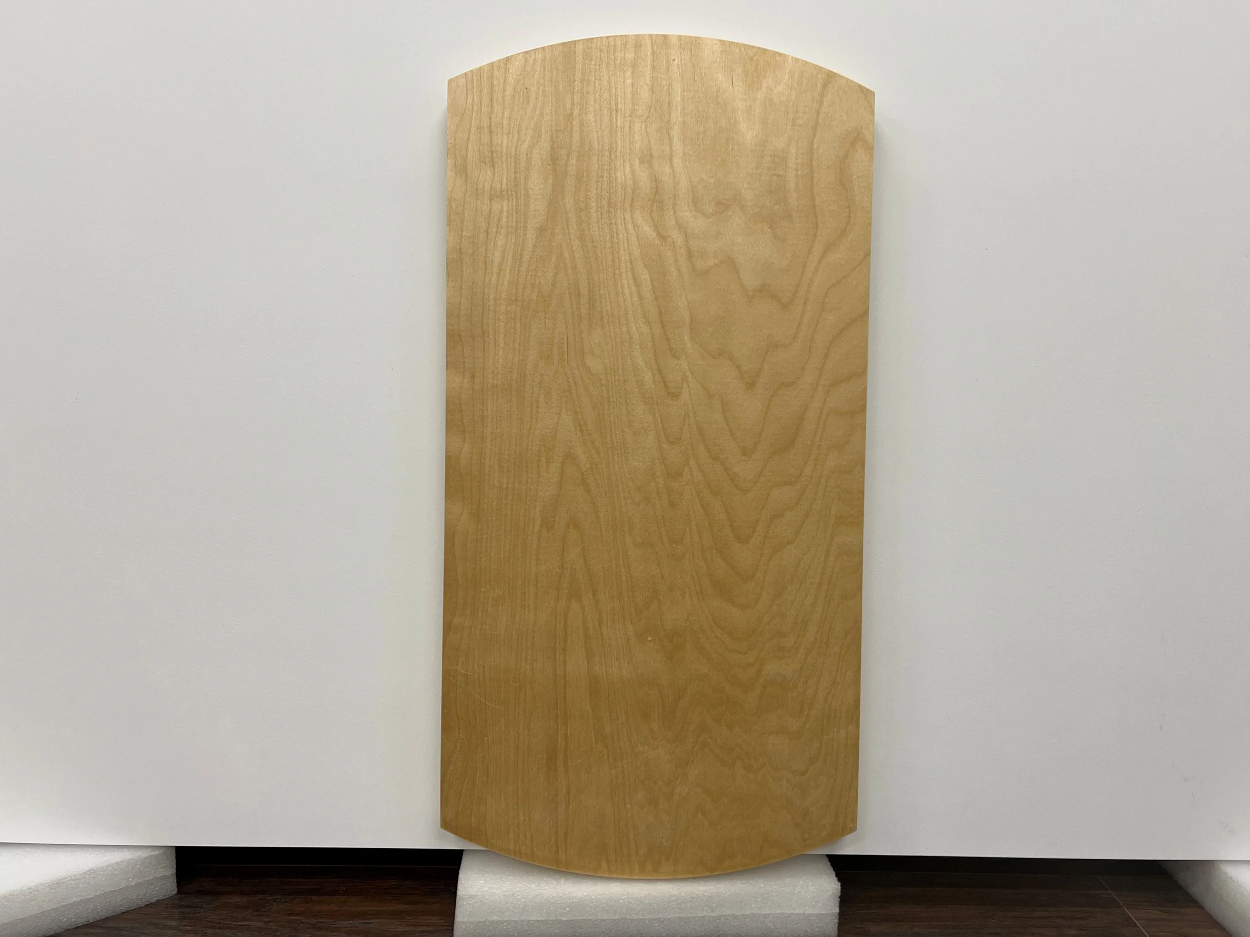 A wooden board with a natural wood grain pattern leaning against a white wall.