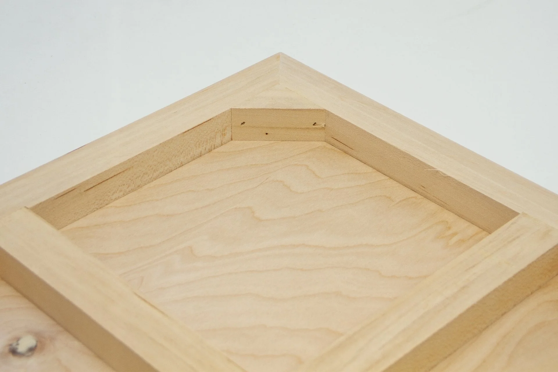 Close-up of unfinished wooden box with beveled edges on a white background.