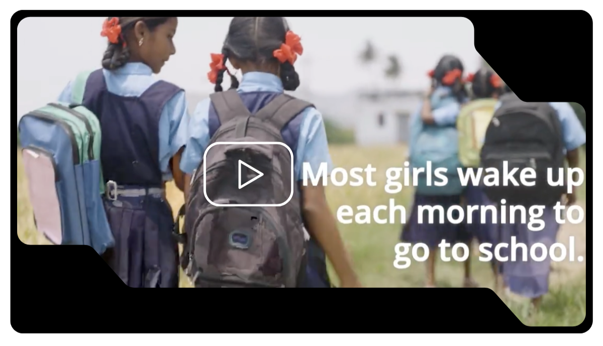Group of young girls walking together with backpacks, some with red ribbons in their hair, in an outdoor school setting, carrying backpacks.