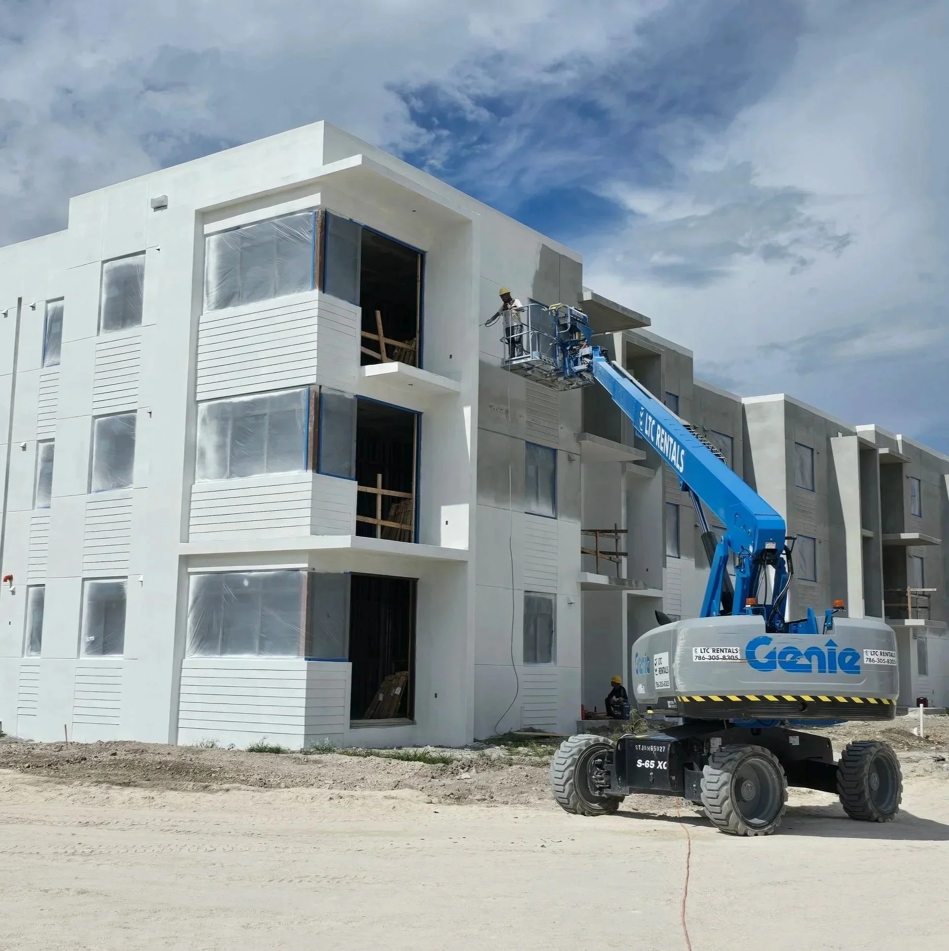 Construction workers on a lift working on a white multi-story building under a partly cloudy sky.