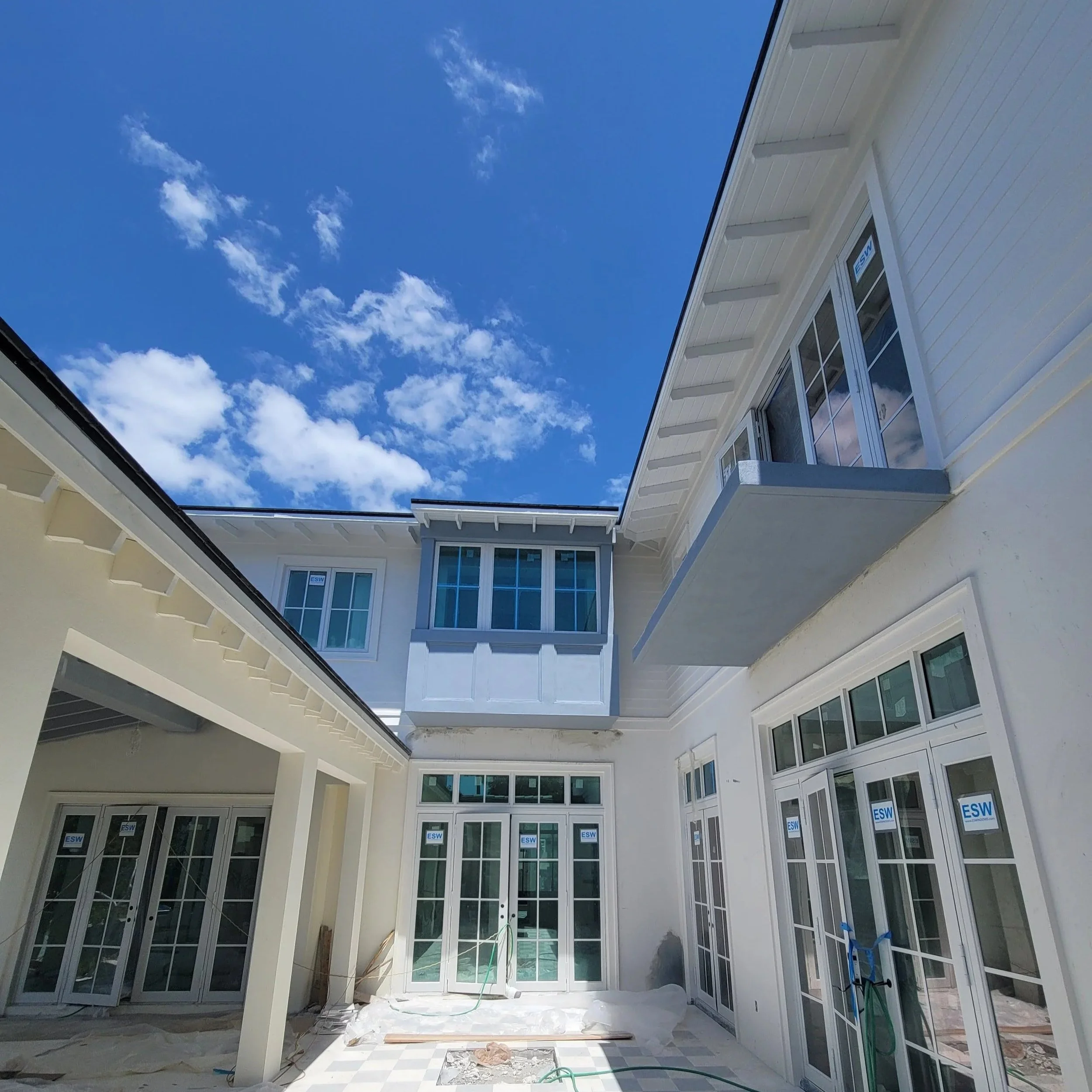 View of a modern house under construction, showing white exterior walls, large glass windows, and a blue sky with clouds.