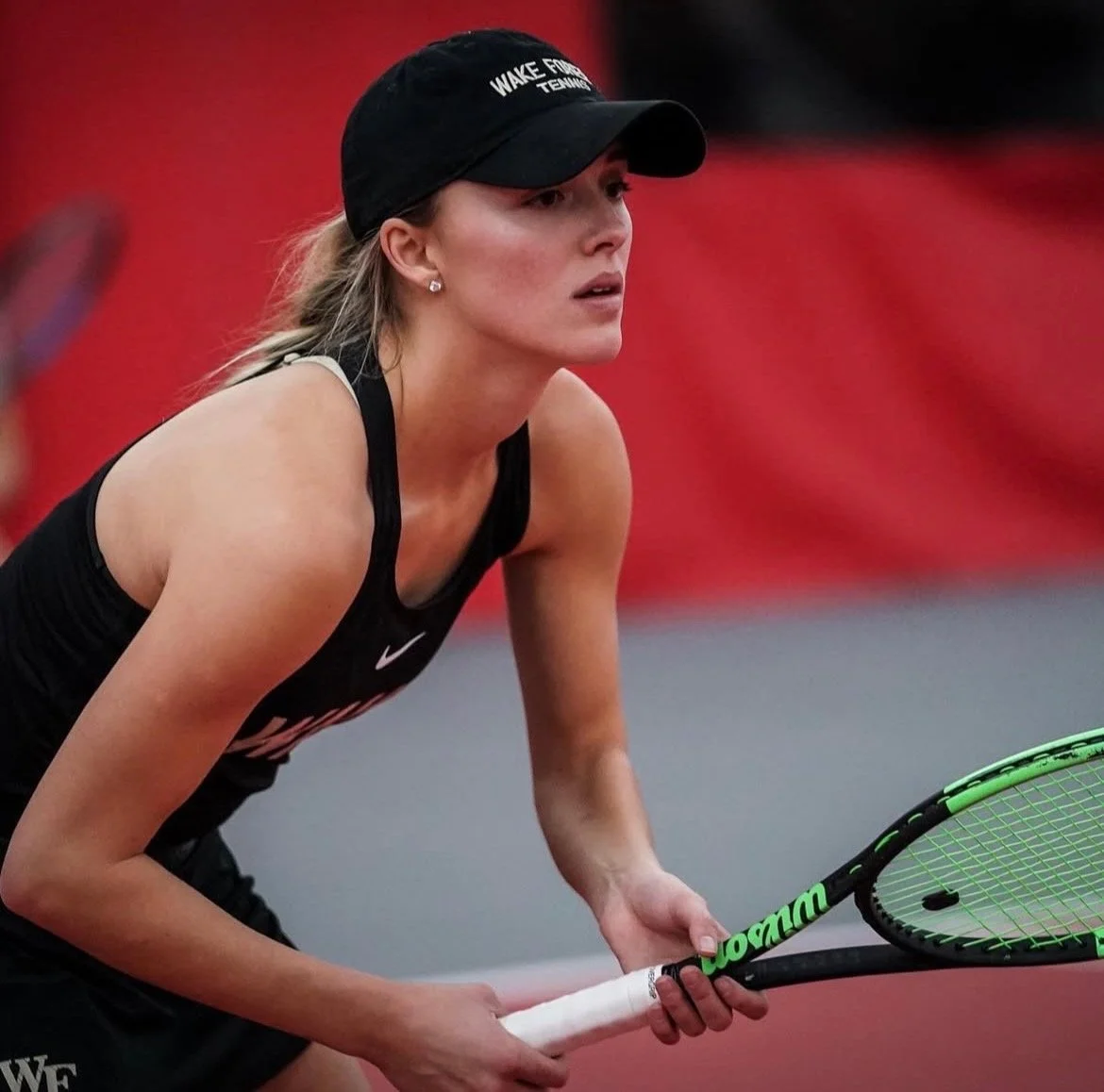 Female tennis player in black athletic wear, wearing a hat, holding a tennis racket during a match.