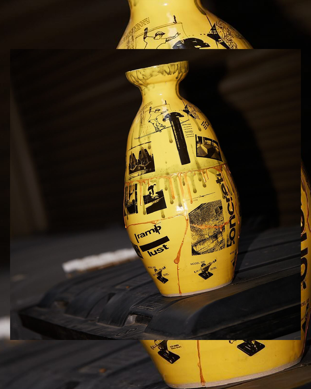 Yellow decorative vase with black text and images, including a man on a seesaw, a screw, and a drill, placed on a black surface with a dark background.