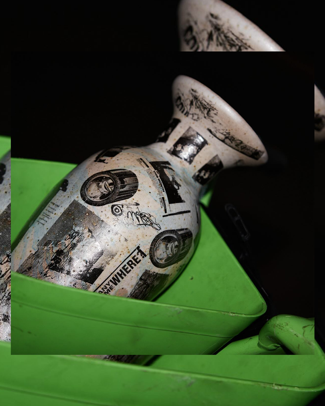 A ceramic vase with graffiti-style black and white artwork, placed inside a bright green plastic container.