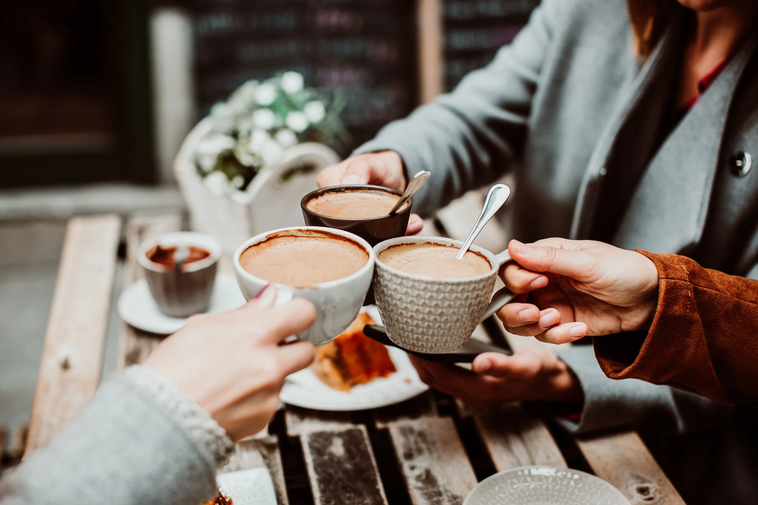 Several people toasting with cups of hot chocolate or coffee at an outdoor table.