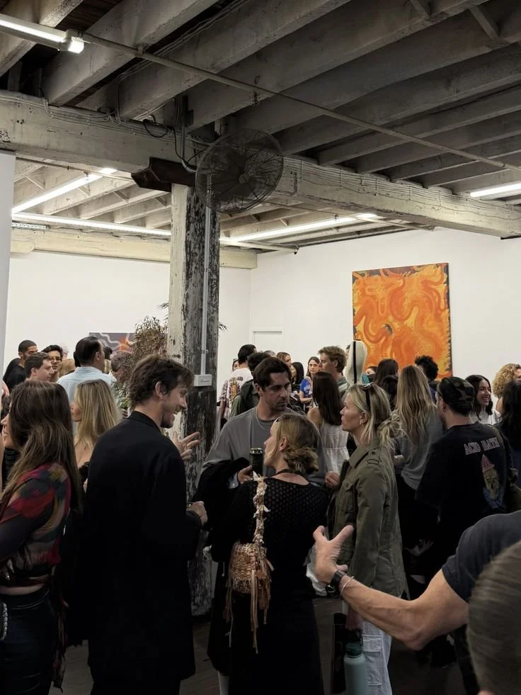 People socializing at an art gallery with a large orange abstract painting on the wall