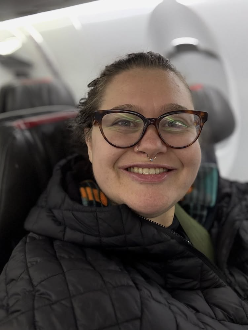 Sophie Keller has glasses and a septum piercing sitting in an airplane seat.