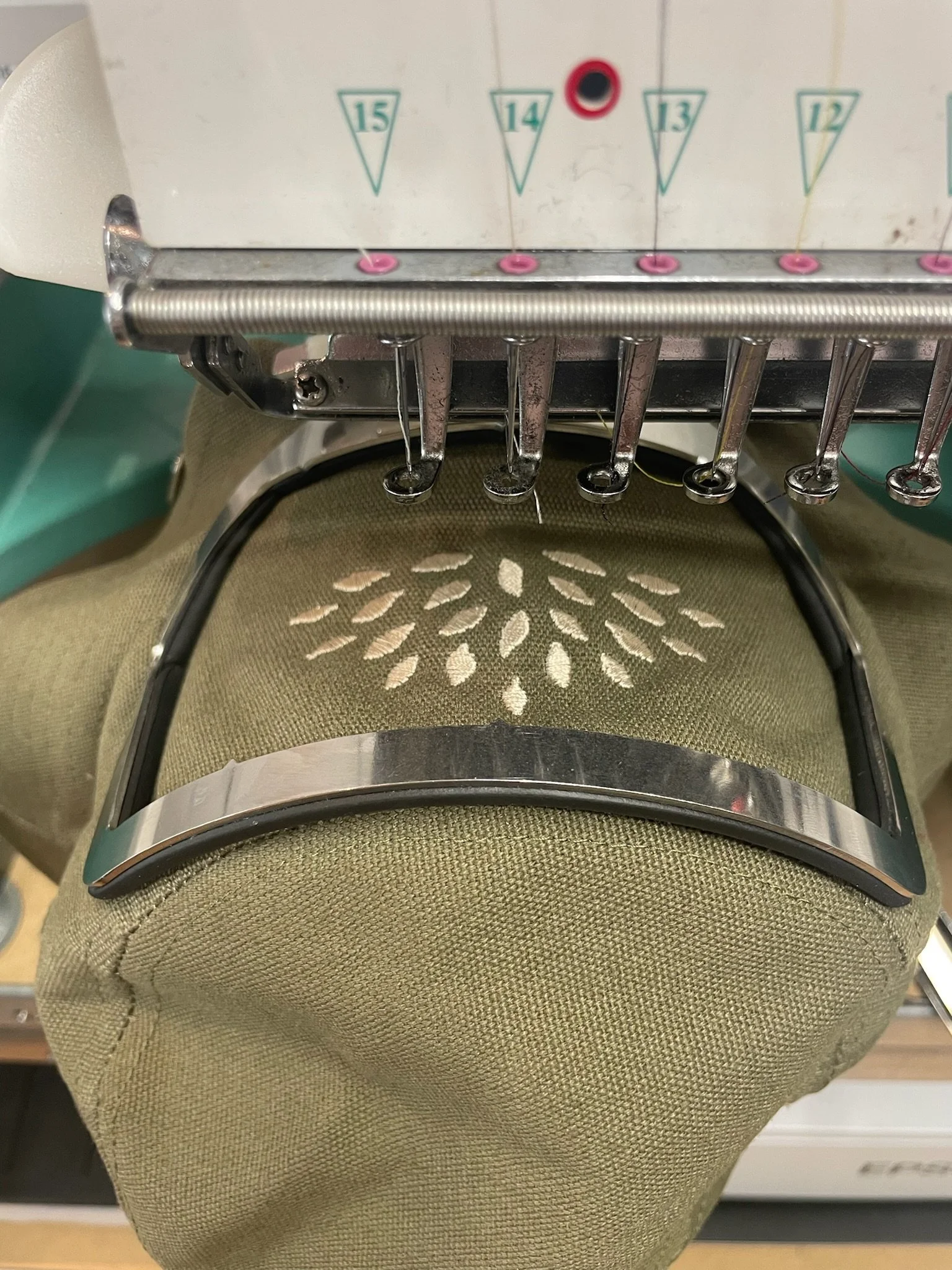 Une machine de couture ou de broderie avec aiguilles et fil, placée sur un fauteuil ou une surface rembourrée verte avec un motif floral brodé.
