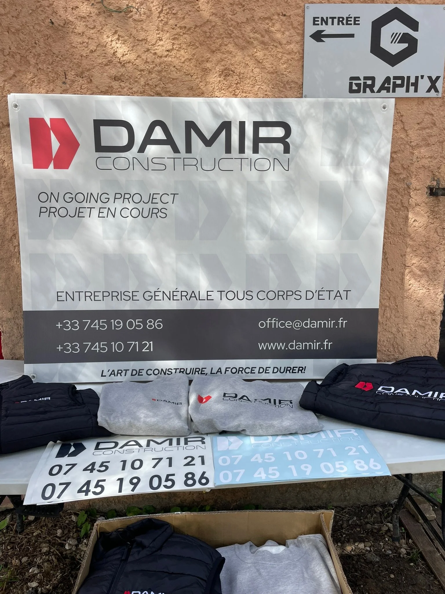 Panneau indiquant un projet en cours de construction par Damir Construction, avec des brochures, t-shirts et vestes à l'effigie de l'entreprise