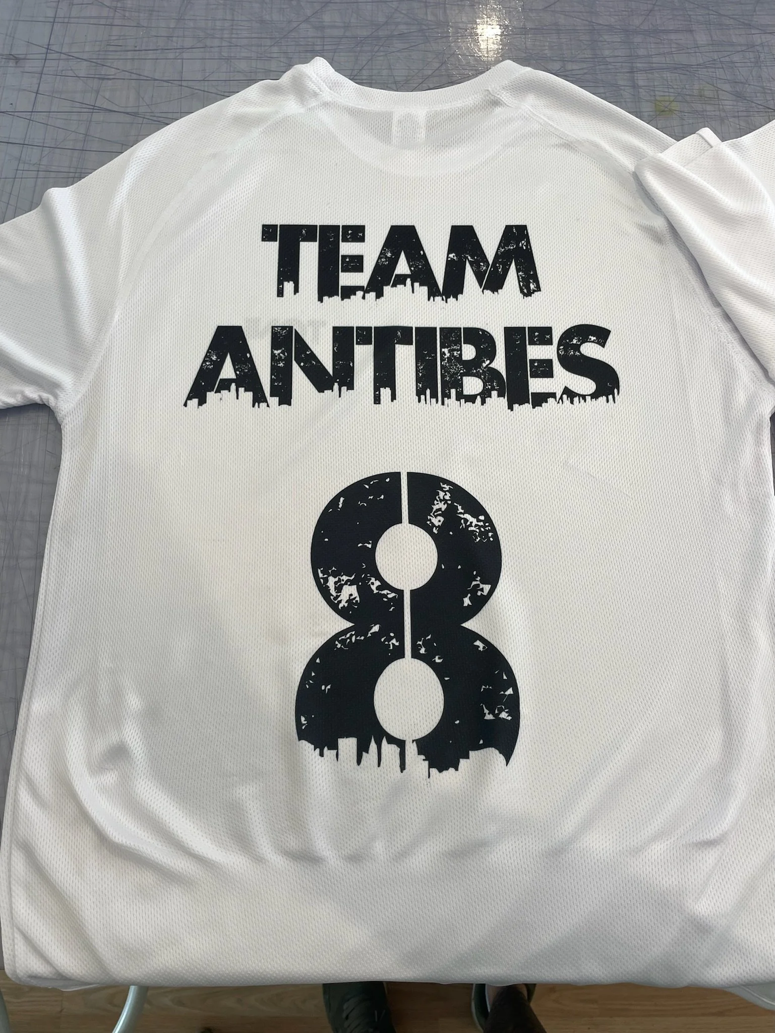 Maillot de sport blanc avec le texte 'TEAM ANTBIES' en noir et un design de chiffre 8