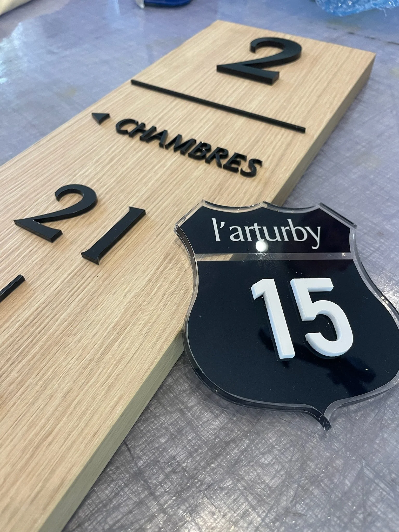 Plaque en bois avec des chiffres et lettres en relief, 2, 15, l'arturby, sur une surface métallique.