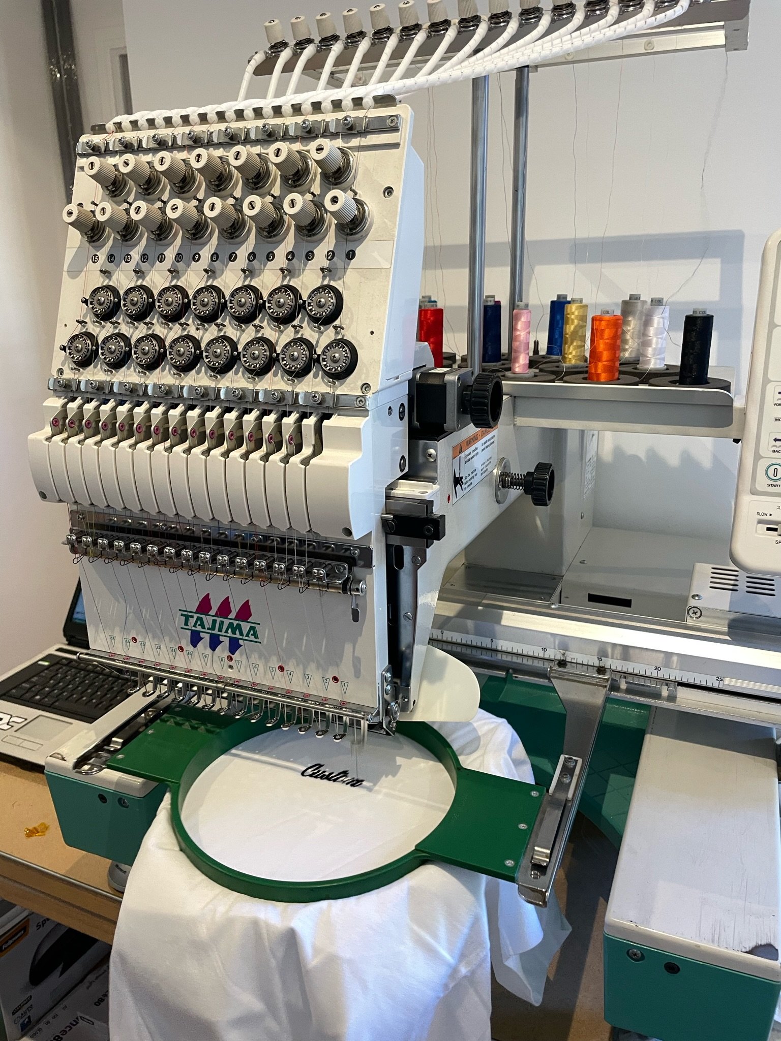 Une machine à broder industrielle avec plusieurs bobines de fil de différentes couleurs, utilisée pour coudre des motifs complexes sur des textiles.