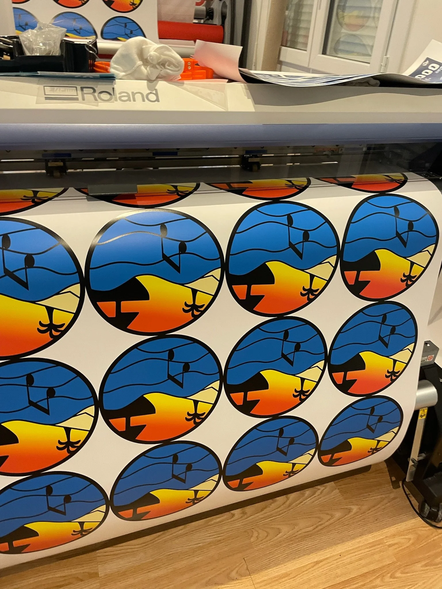 Une imprimante à sublimation imprime un motif coloré de cercles représentant un paysage avec un coucher de soleil, des montagnes et un arbre.