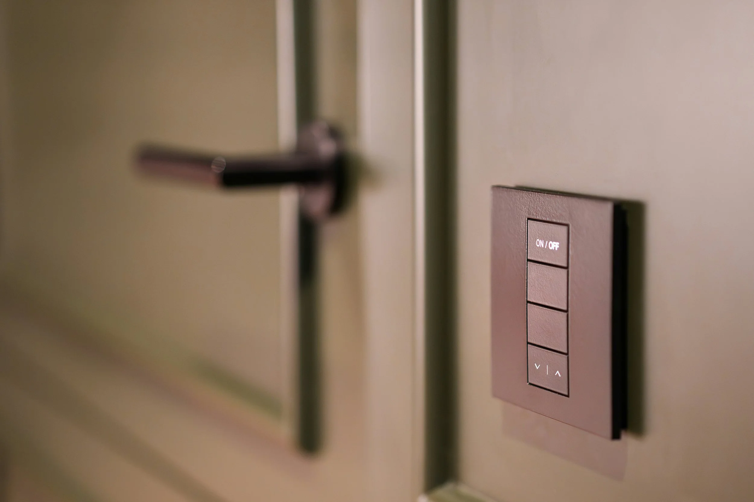 Close-up of a wall with a metallic switch panel featuring an 'On/Off' button and arrow buttons, alongside a metallic door handle.