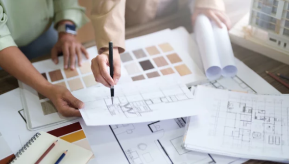 Two people examining architectural blueprints on a table, with color swatches and rolled-up blueprints nearby.