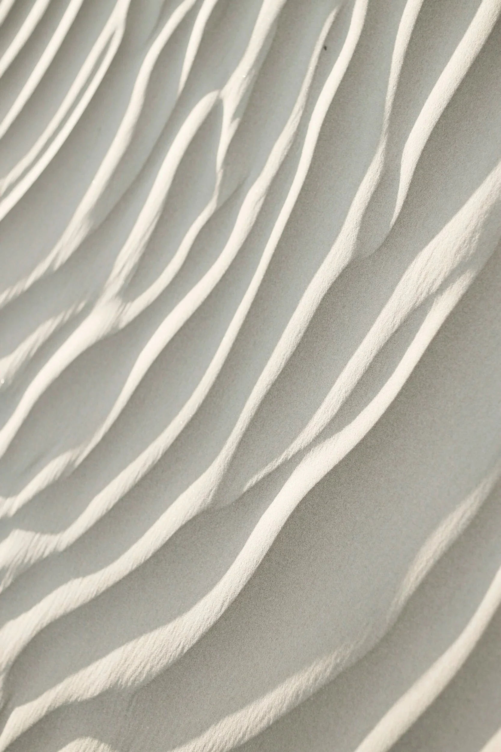 Close-up of white wavy textured wall or surface with shadows highlighting the raised patterns.