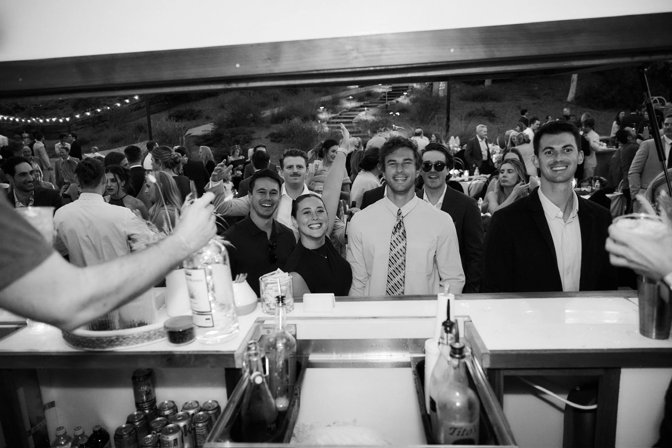 Group of people smiling and enjoying a party at the bar with a crowd in the background, black and white photo.