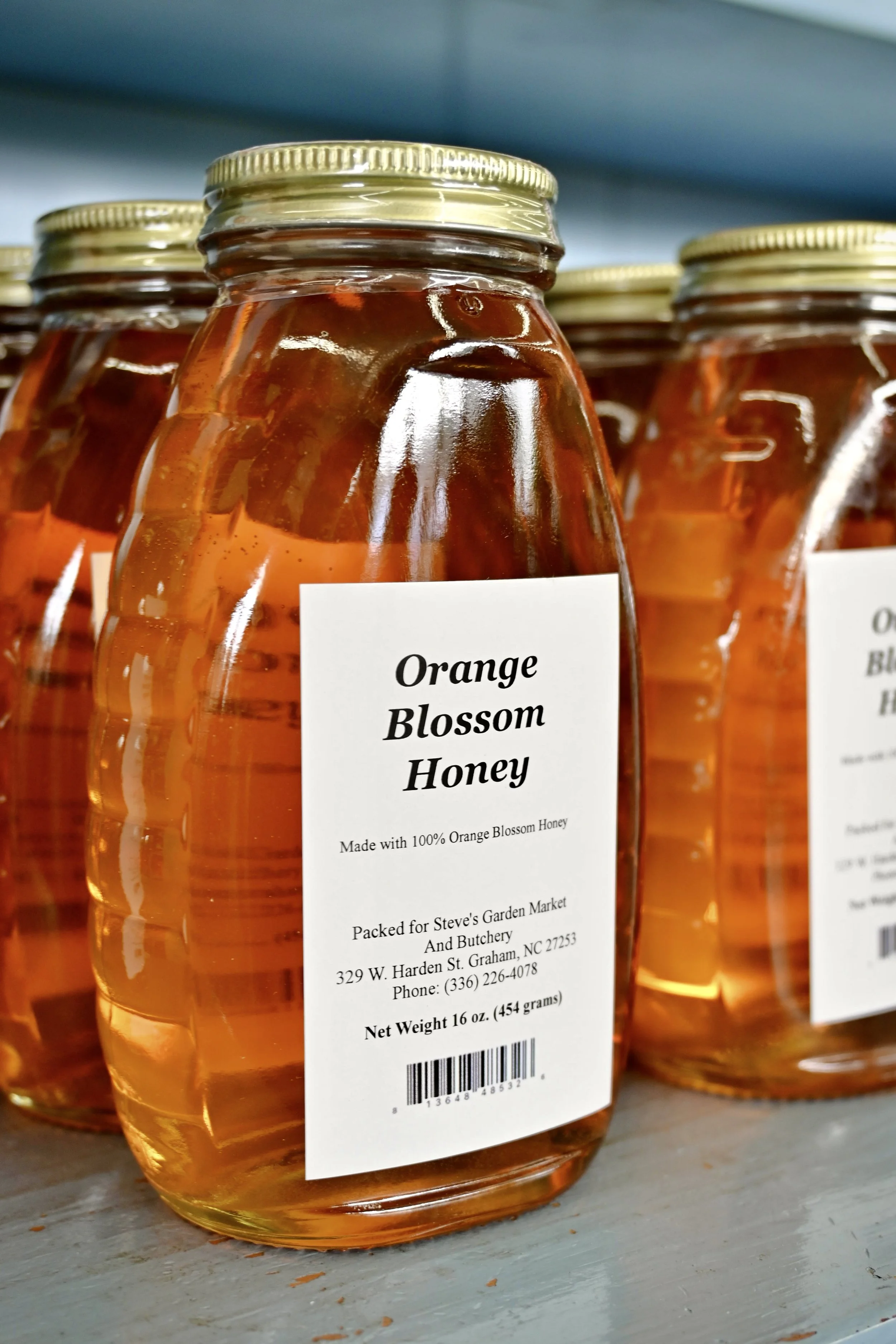 A jar of orange blossom honey with a label indicating it is made with 100% orange blossom honey, packed at Steve's Garden Market in Graham, North Carolina.