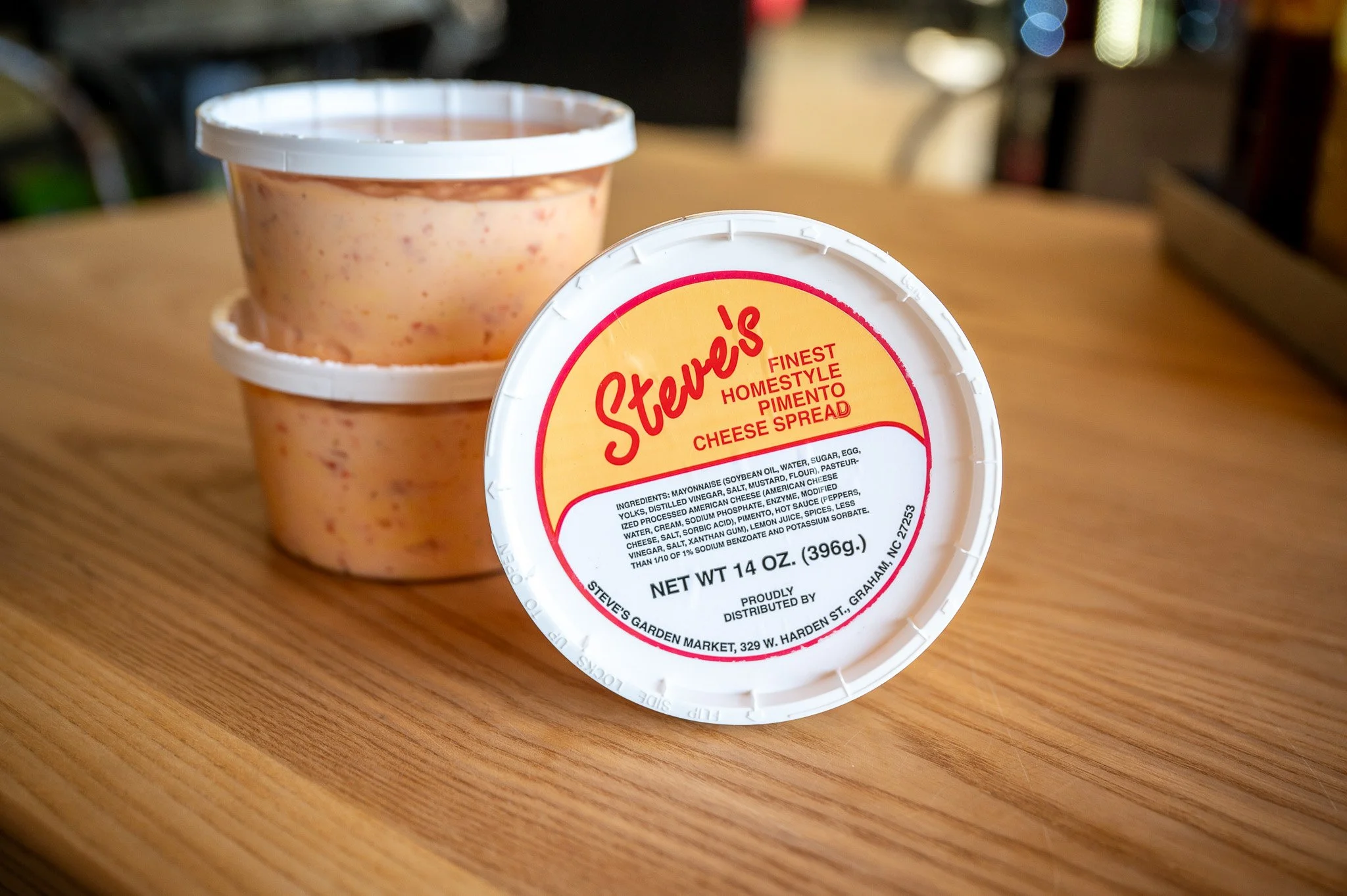 Two containers of Steve's cheese spread, with the top one showing ingredients, placed on a wooden table.