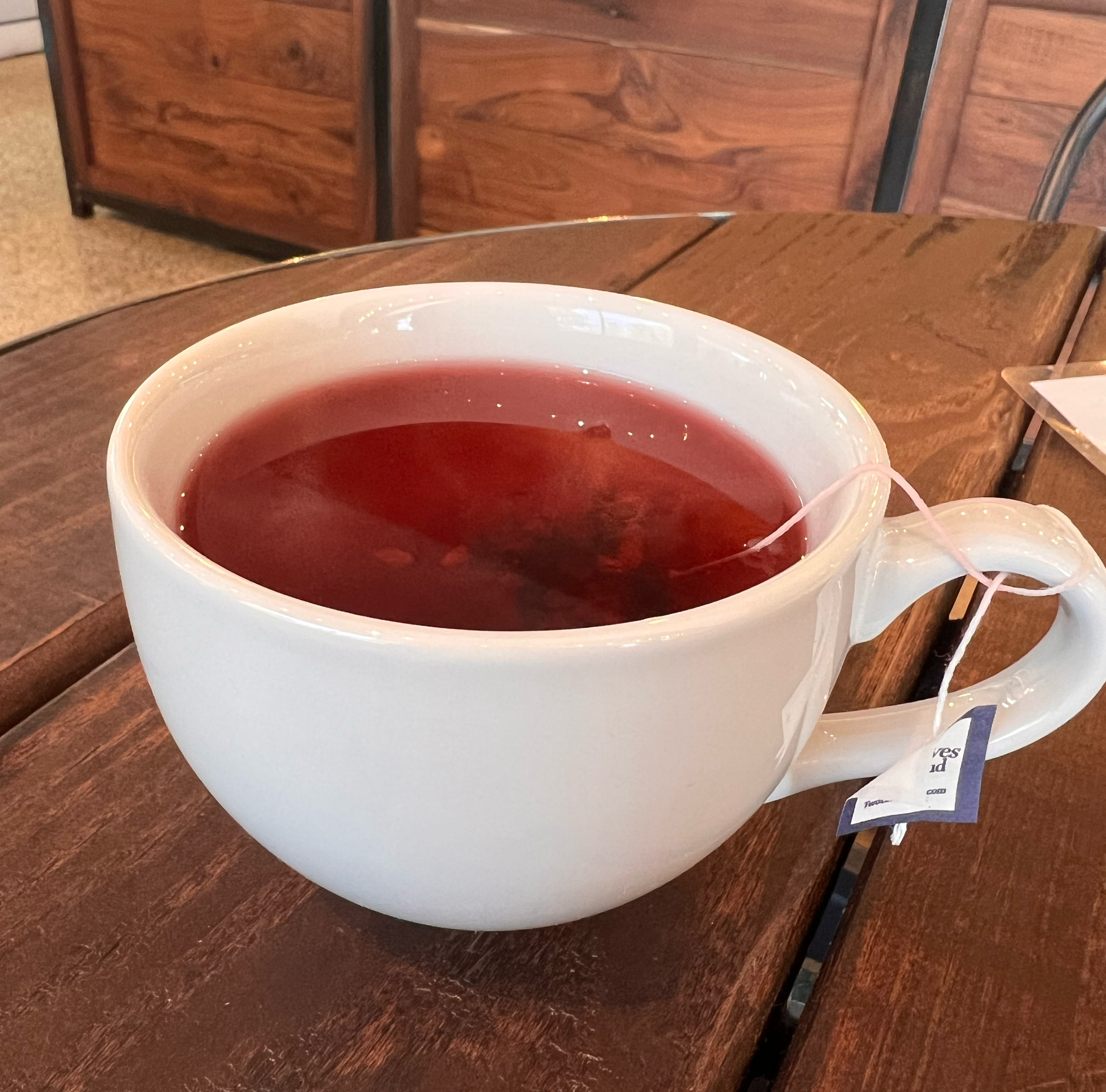 A white mug filled with red tea sitting on a wooden table.