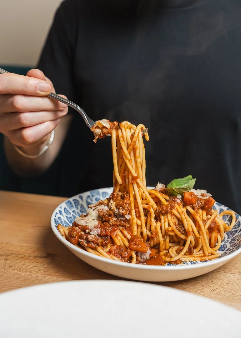 Person qui mange des spaghetti bolognaise dans une assiette en céramique blanche et bleue.