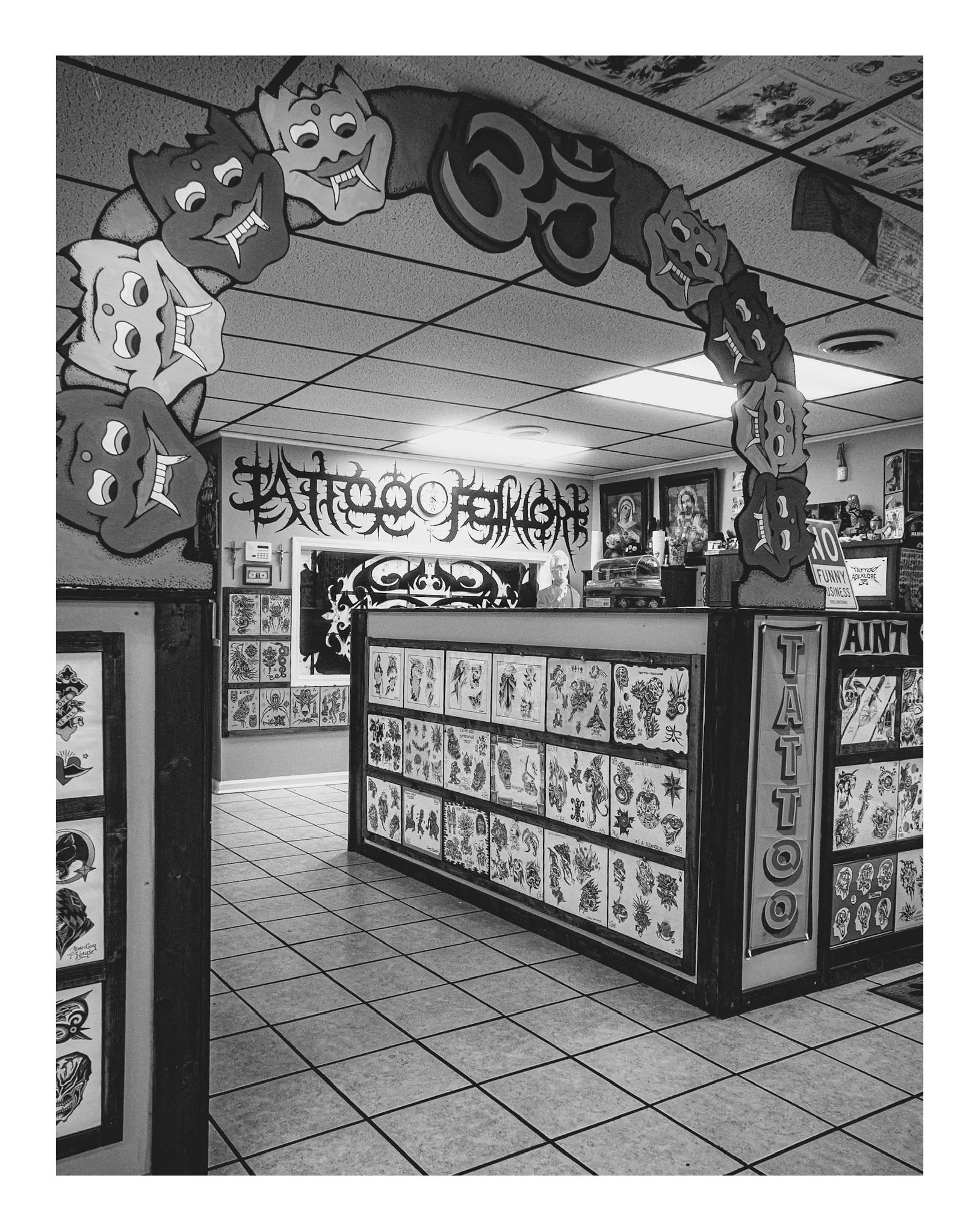 Tattoo shop interior with tattoo flash art displayed on panels, patterned tile flooring, and Halloween-themed hanging decorations.