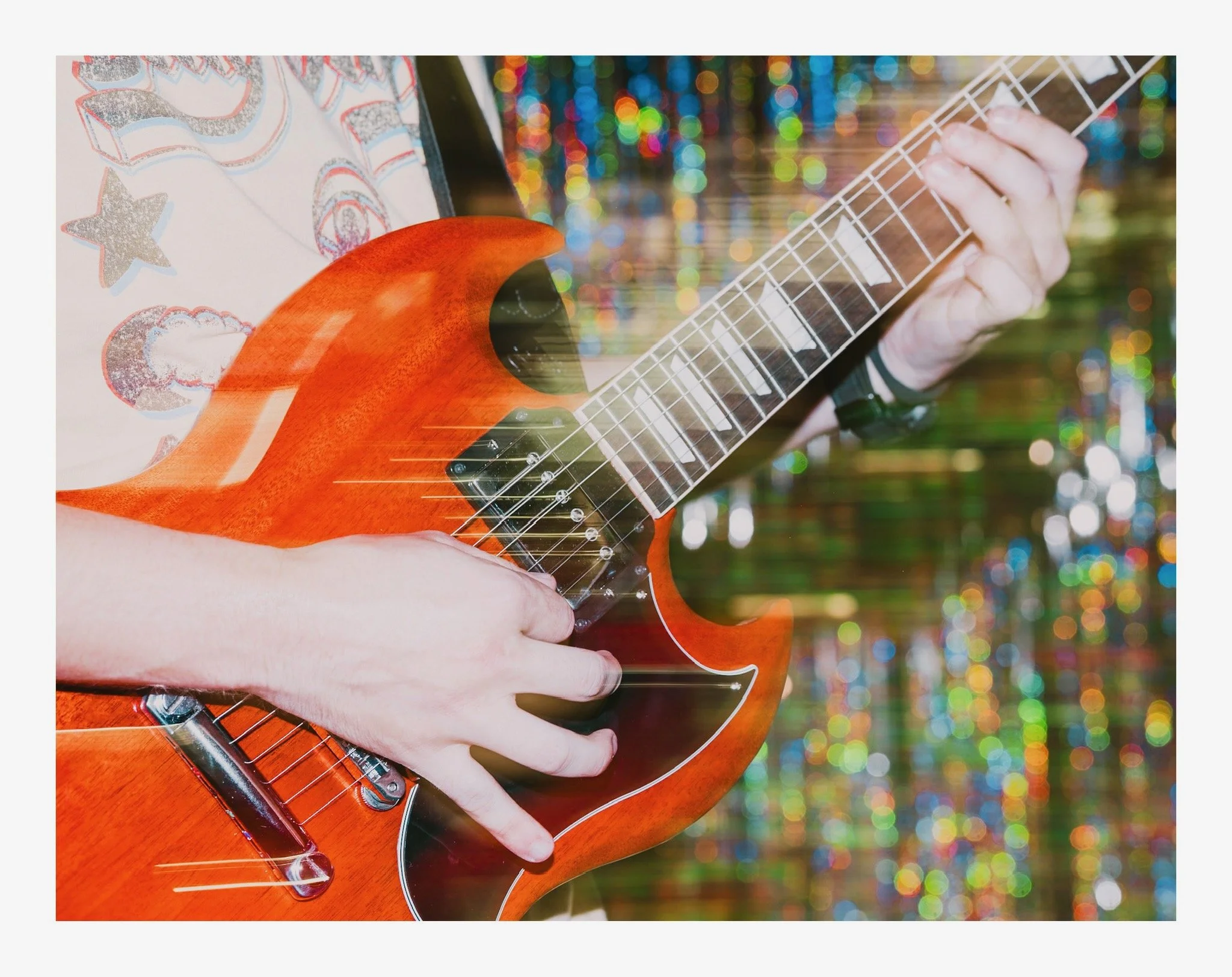 Close-up of a person's hand playing an electric guitar with a colorful, blurred background.