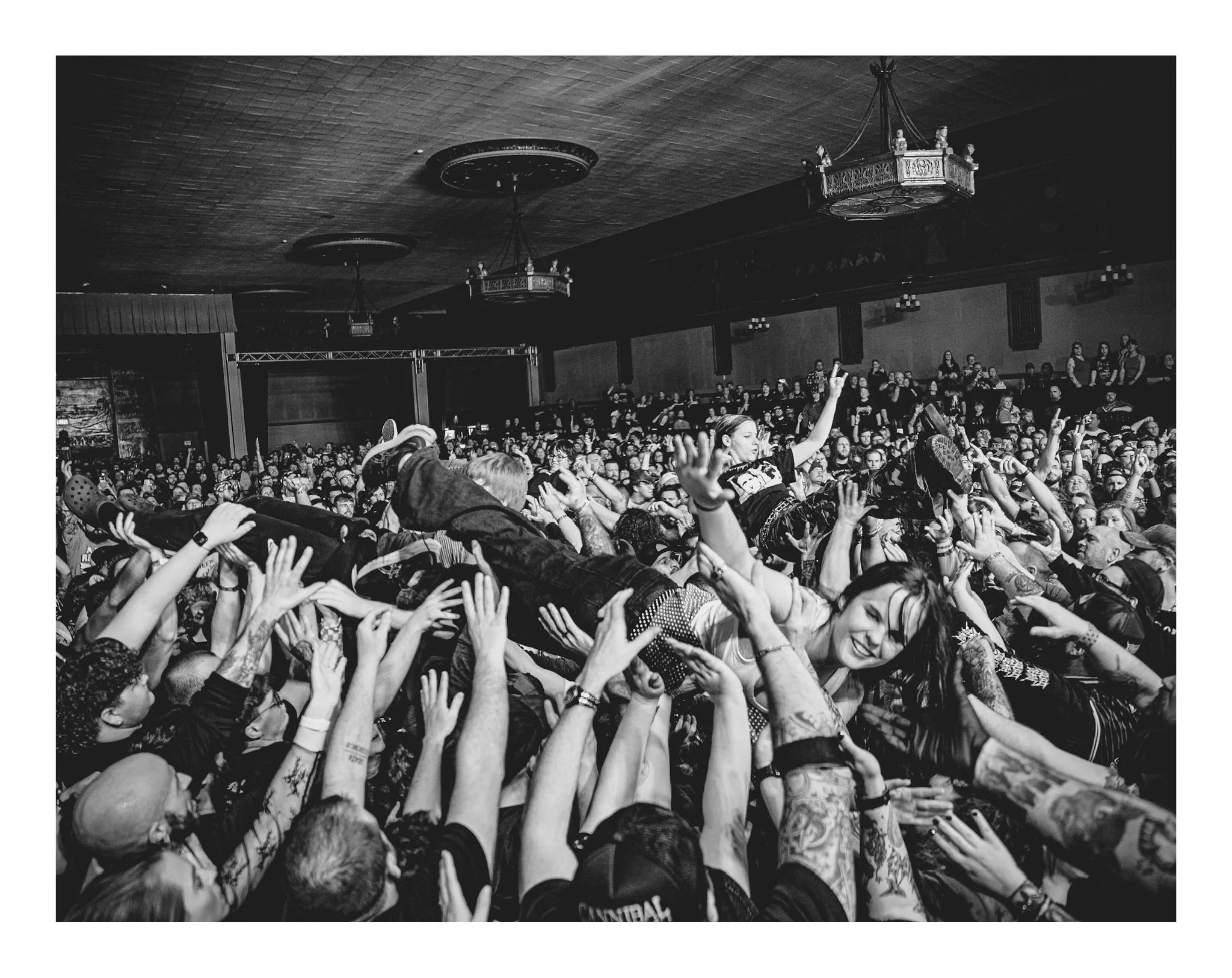 Crowd of people at a concert or event, with many raising their hands and engaging with the performers on stage.