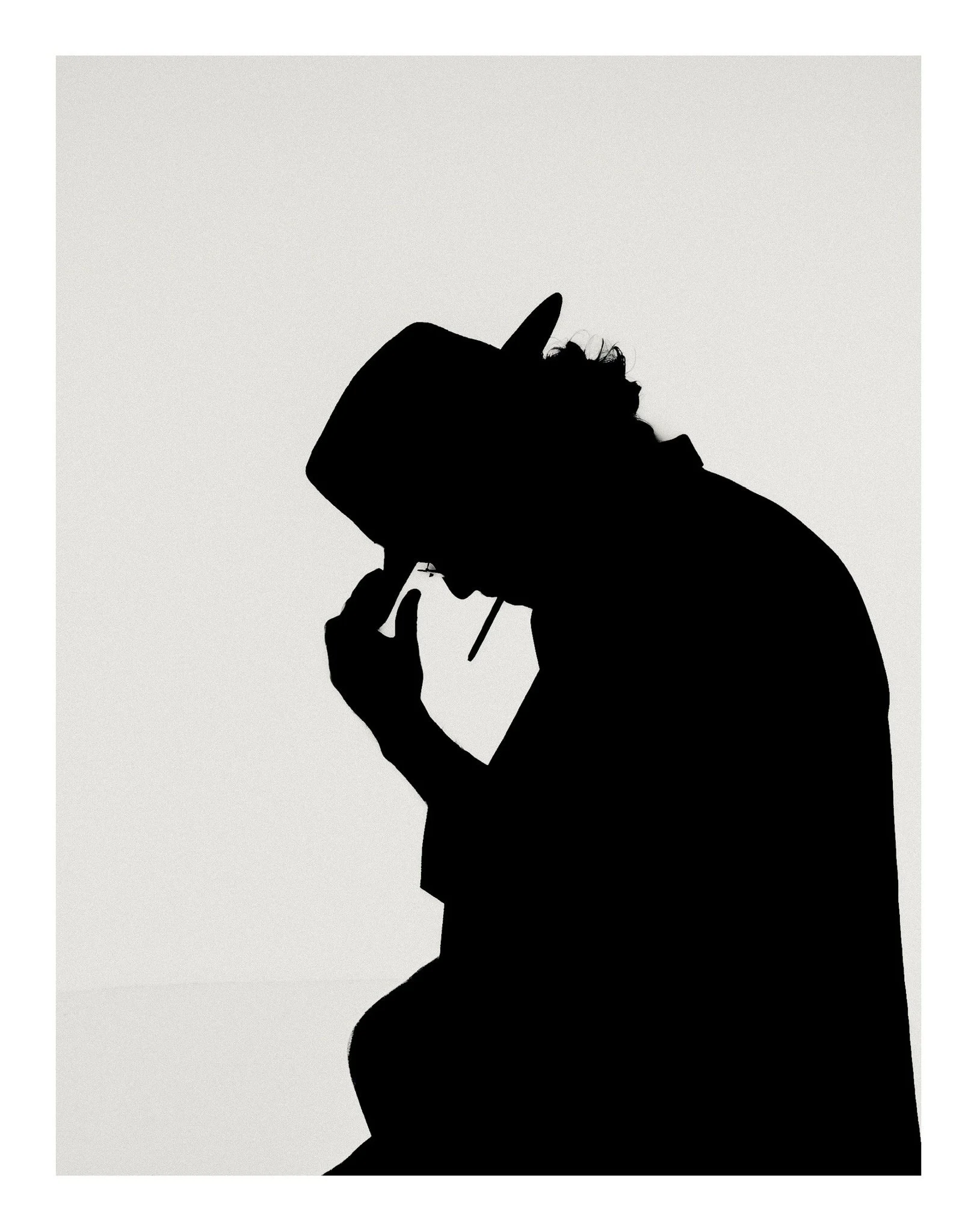 Silhouette of a person wearing a hat, touching their face, against a plain background.